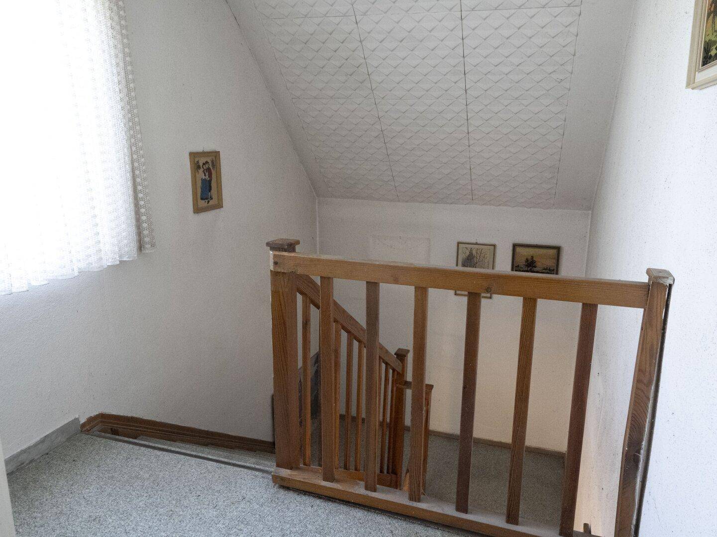 Treppenhaus mit Holzgeländer, das in die untere Etage führt, mit heller Wandgestaltung.