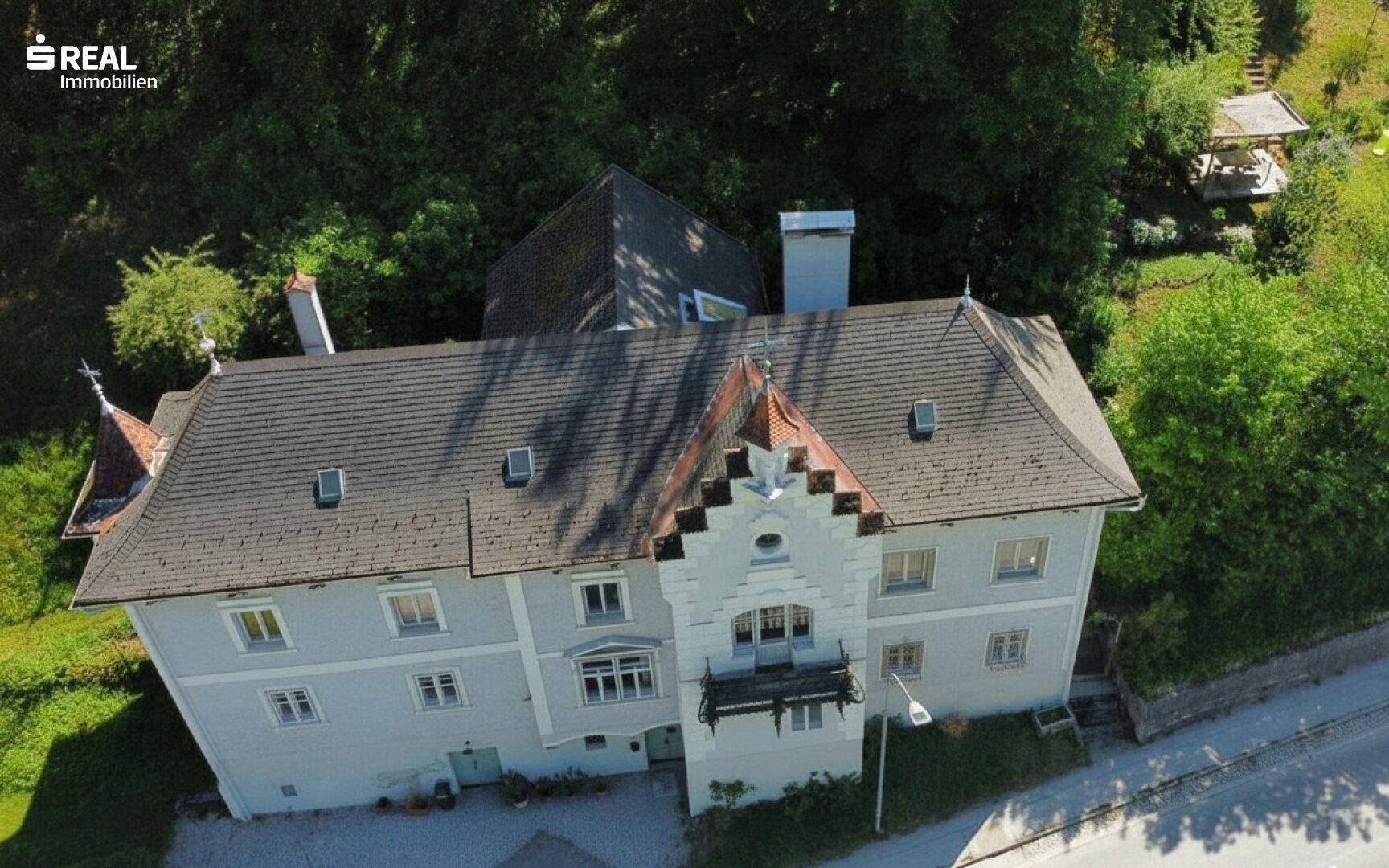 Historisches Anwesen aus der Vogelperspektive, eingebettet in eine grüne Hügellandschaft mit altem Baumbestand.