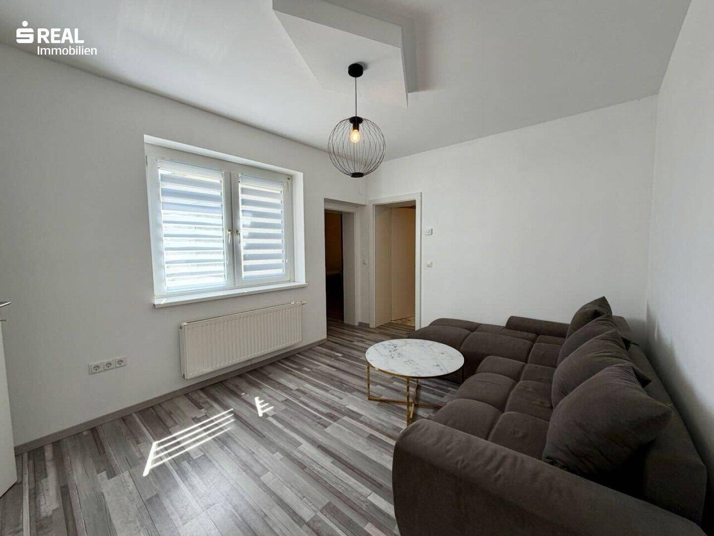 Gemütliches Wohnzimmer mit modernem Laminatboden, bequemer Couch und stilvoller Beleuchtung.