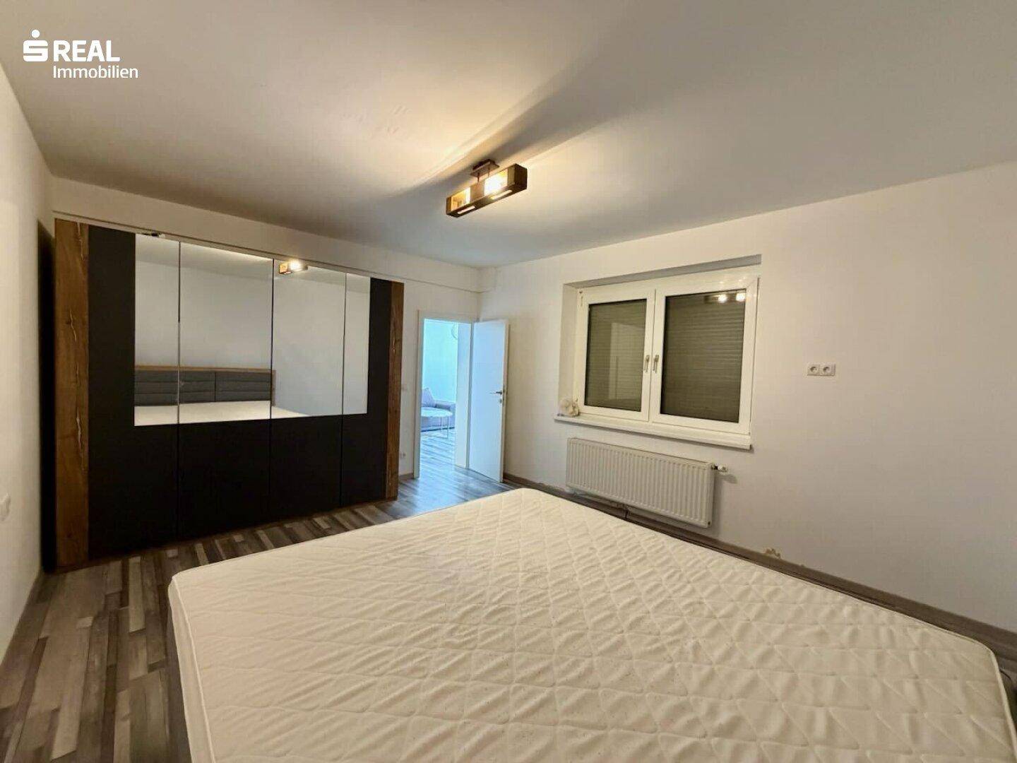 Schlafzimmer mit Laminatboden, großem Spiegelschrank und ausreichend Platz für ein Doppelbett.