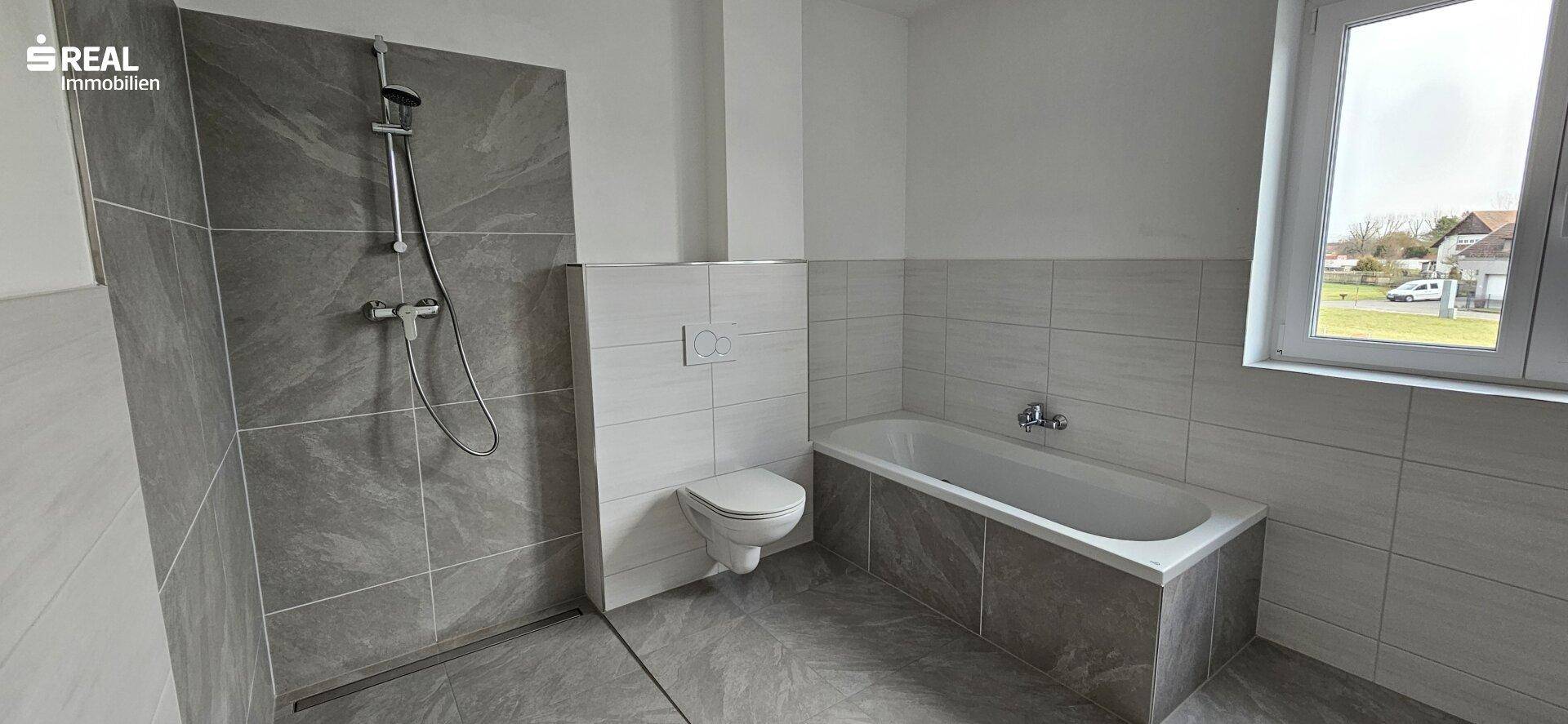 Geräumiges Badezimmer mit Badewanne, separater Dusche, wandhängendem WC und Fenster.