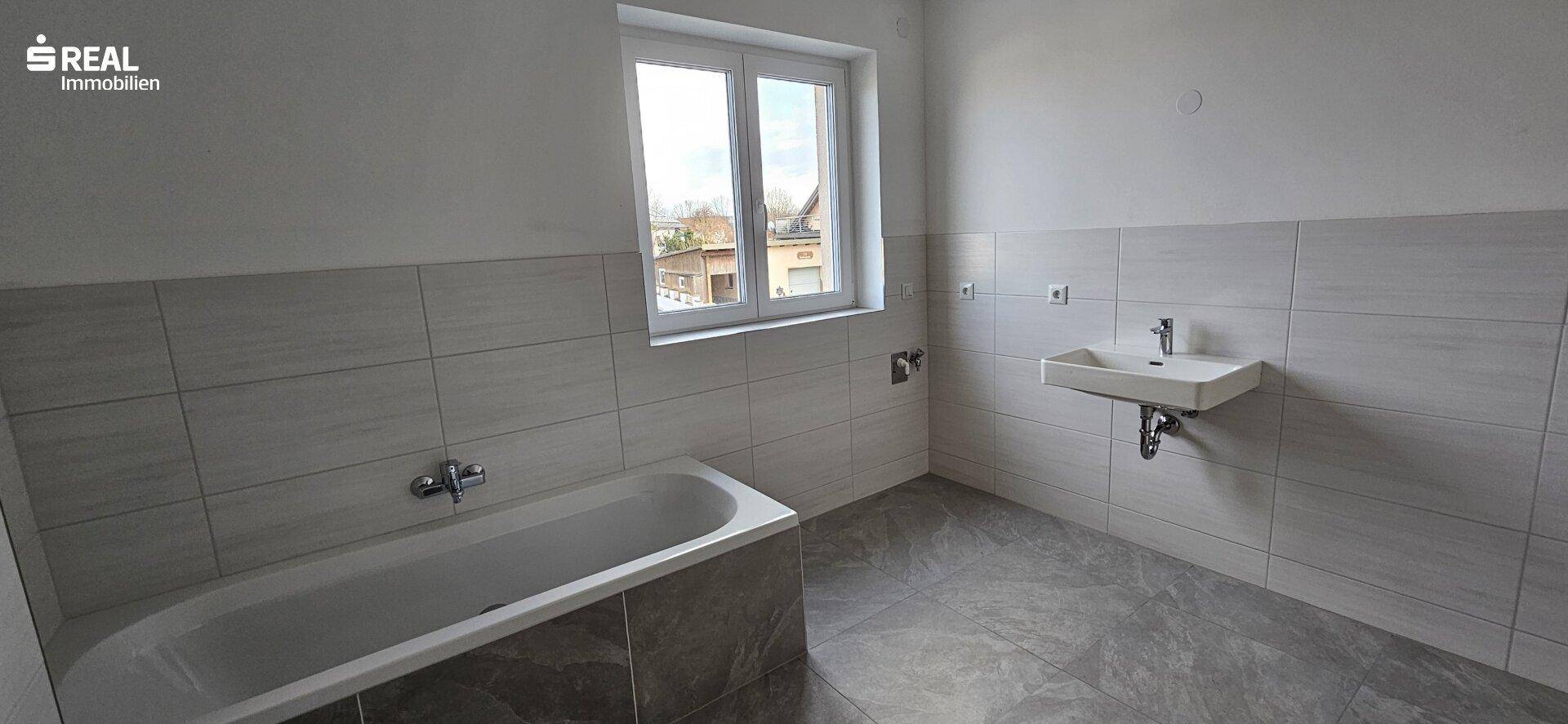 Helles Badezimmer mit Badewanne, Waschbecken und Fenster, das viel Tageslicht bietet.
