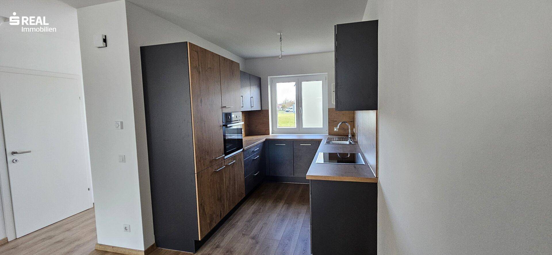 Moderne Küche mit dunklen Schränken, Holzoptik-Arbeitsplatten und einem Fenster für Tageslicht.