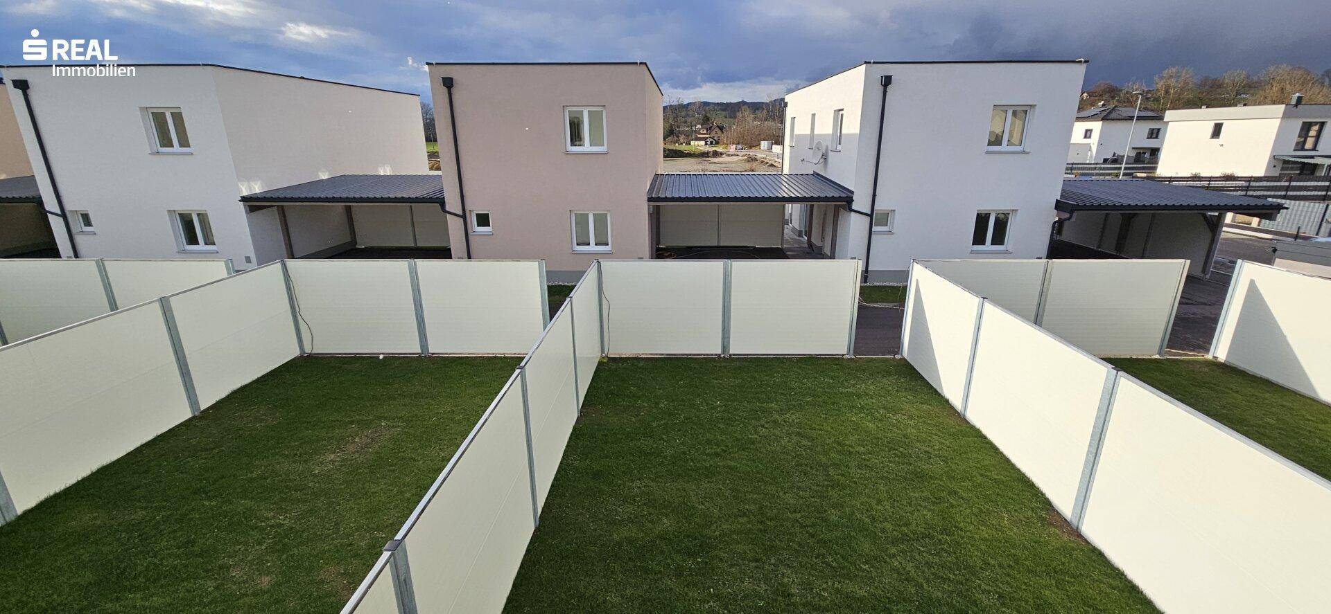 Blick von oben auf mehrere private Gärten mit Rasenflächen und hohen Sichtschutzzäunen.