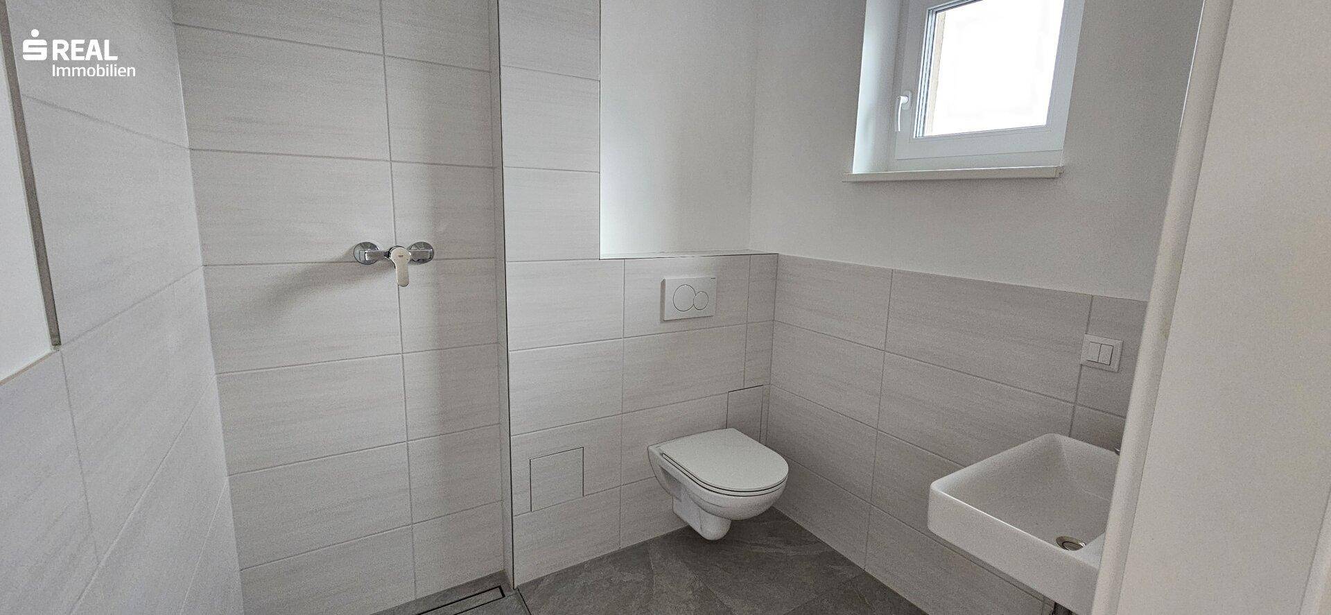 Modernes Badezimmer mit ebenerdiger Dusche, wandhängendem WC und kleinem Waschbecken.