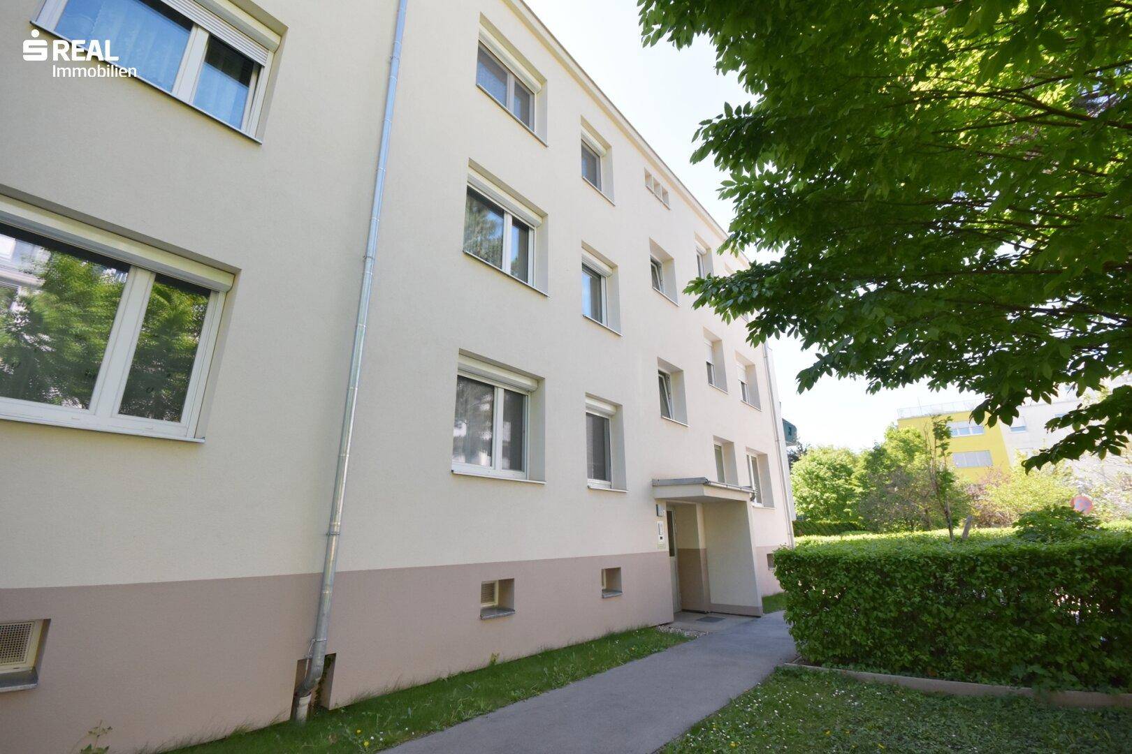 Seitenansicht eines Wohngebäudes mit mehreren Fenstern, Eingangsbereich und gepflegter Hecke.
