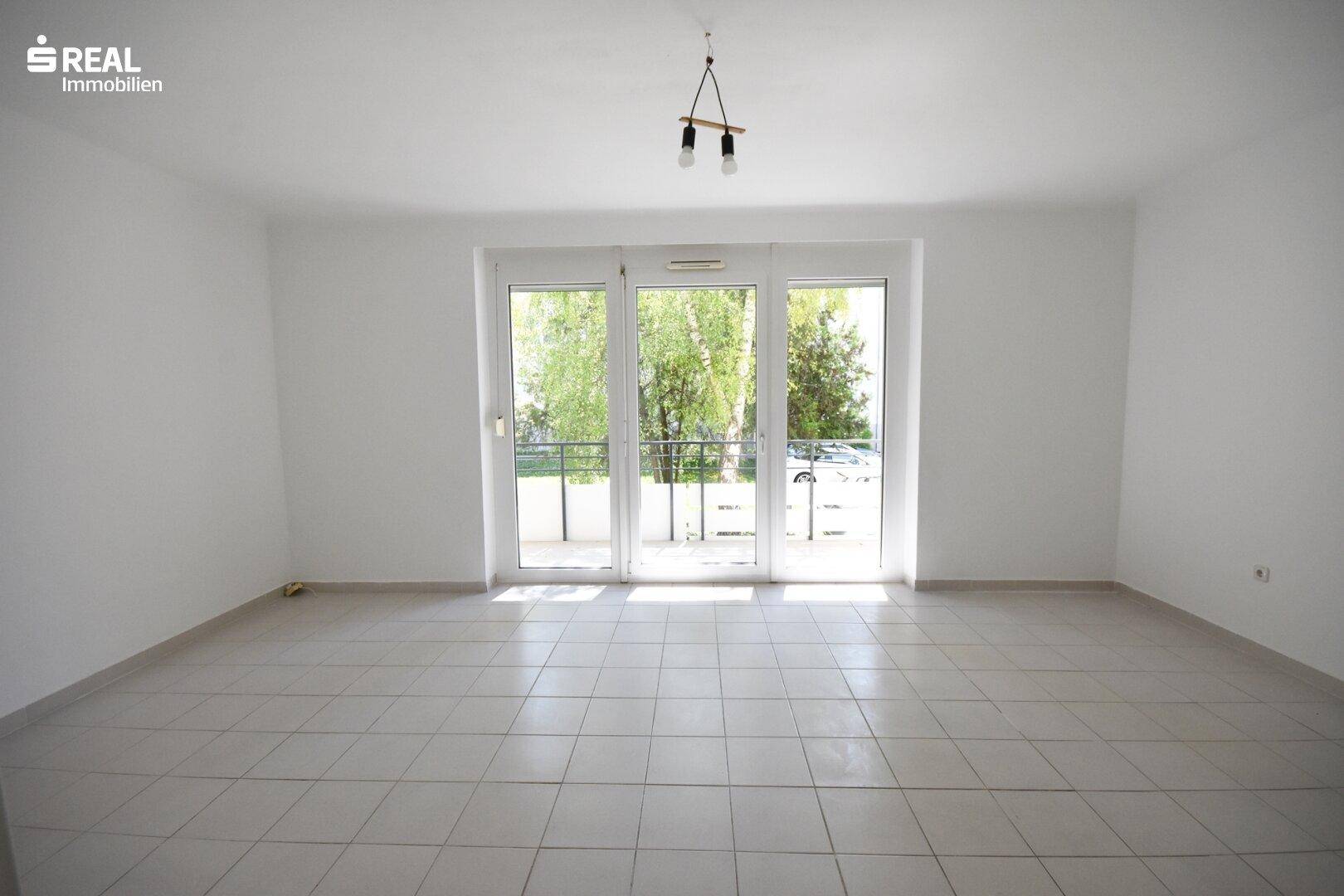Geräumiges, helles Wohnzimmer mit Fliesenboden und großen Glastüren zum Außenbereich.
