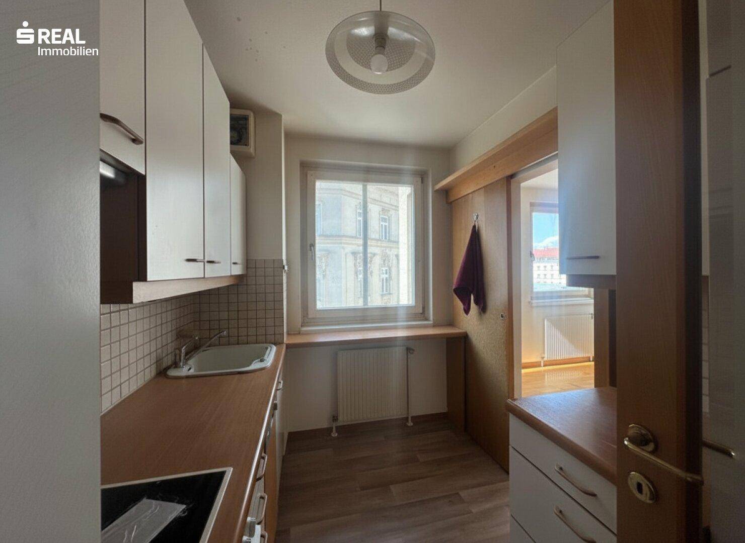 Funktionale Küche mit Holztheke, Fliesenrückwand und Fenster, das Tageslicht hereinlässt.