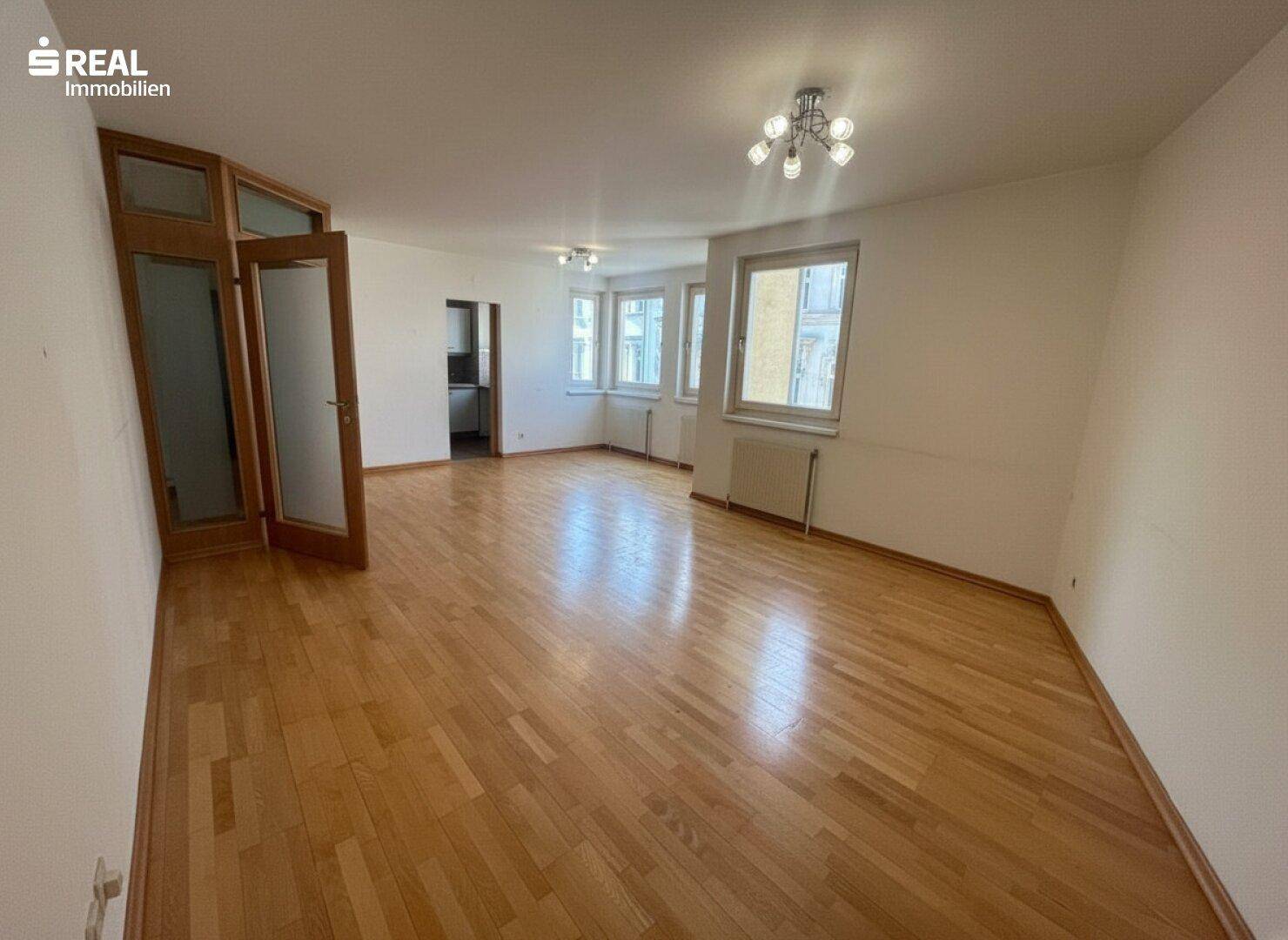 Geräumiges, leeres Wohn- und Esszimmer mit Holzboden und mehreren Fenstern.