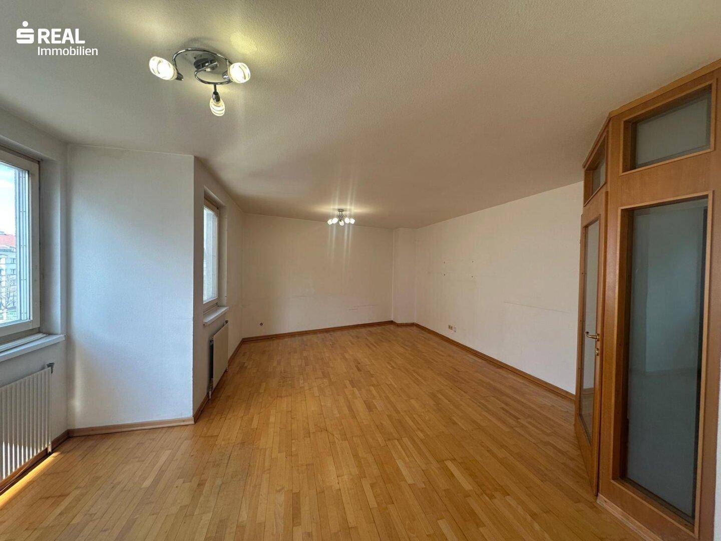 Heller, leerer Wohnbereich mit Holzboden und großen Fenstern, bereit zur individuellen Gestaltung.