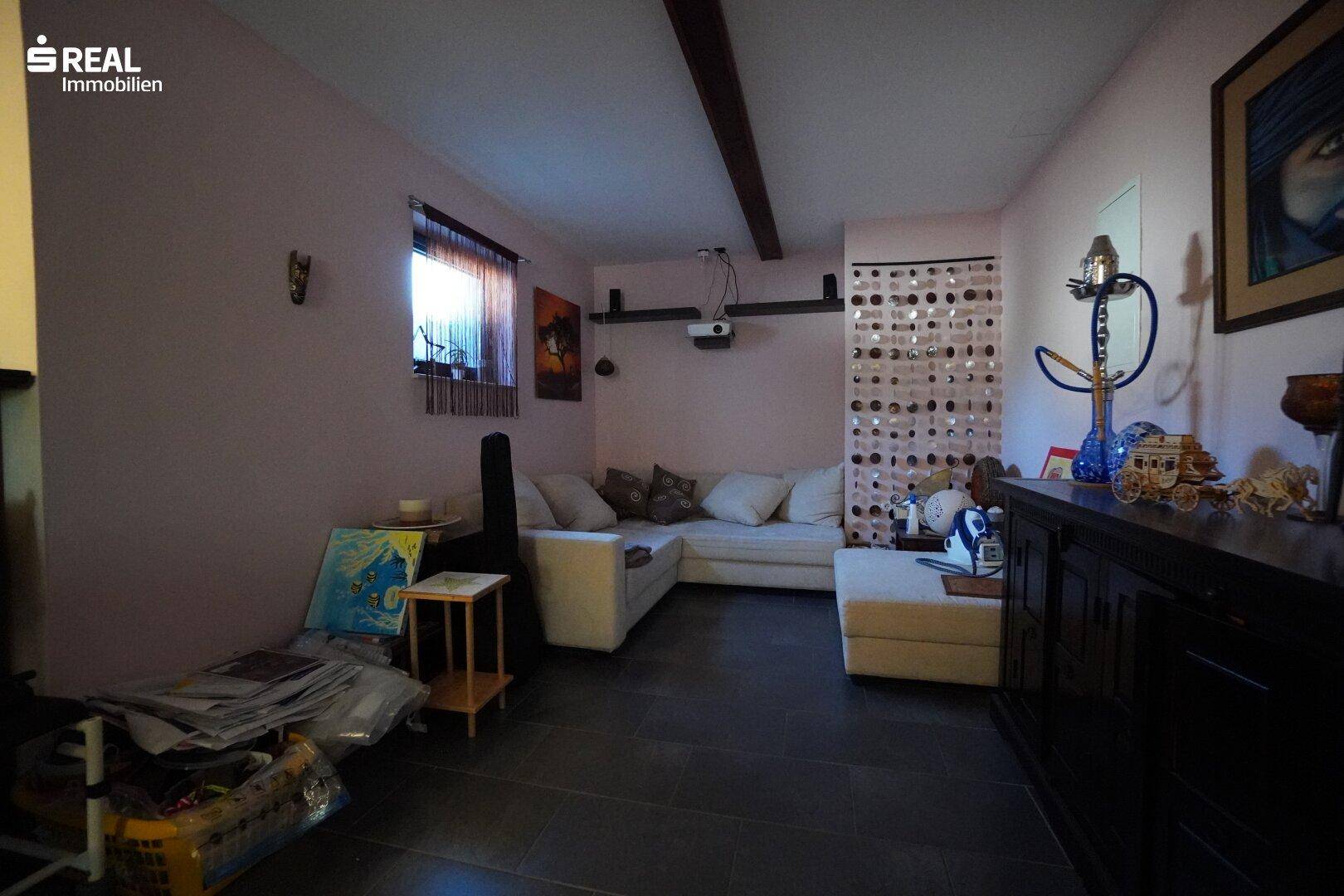 Gemütliches Wohnzimmer im Untergeschoss mit Sofa und dunklem Fliesenboden.