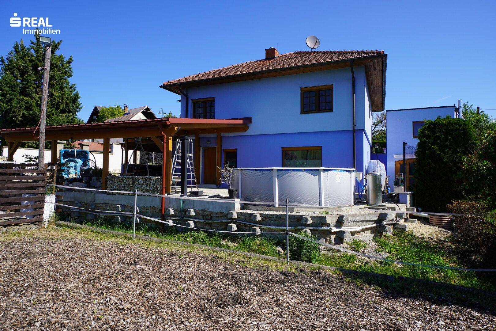 Rückseite des Hauses mit überdachtem Bereich und einem Aufstellpool im Garten.