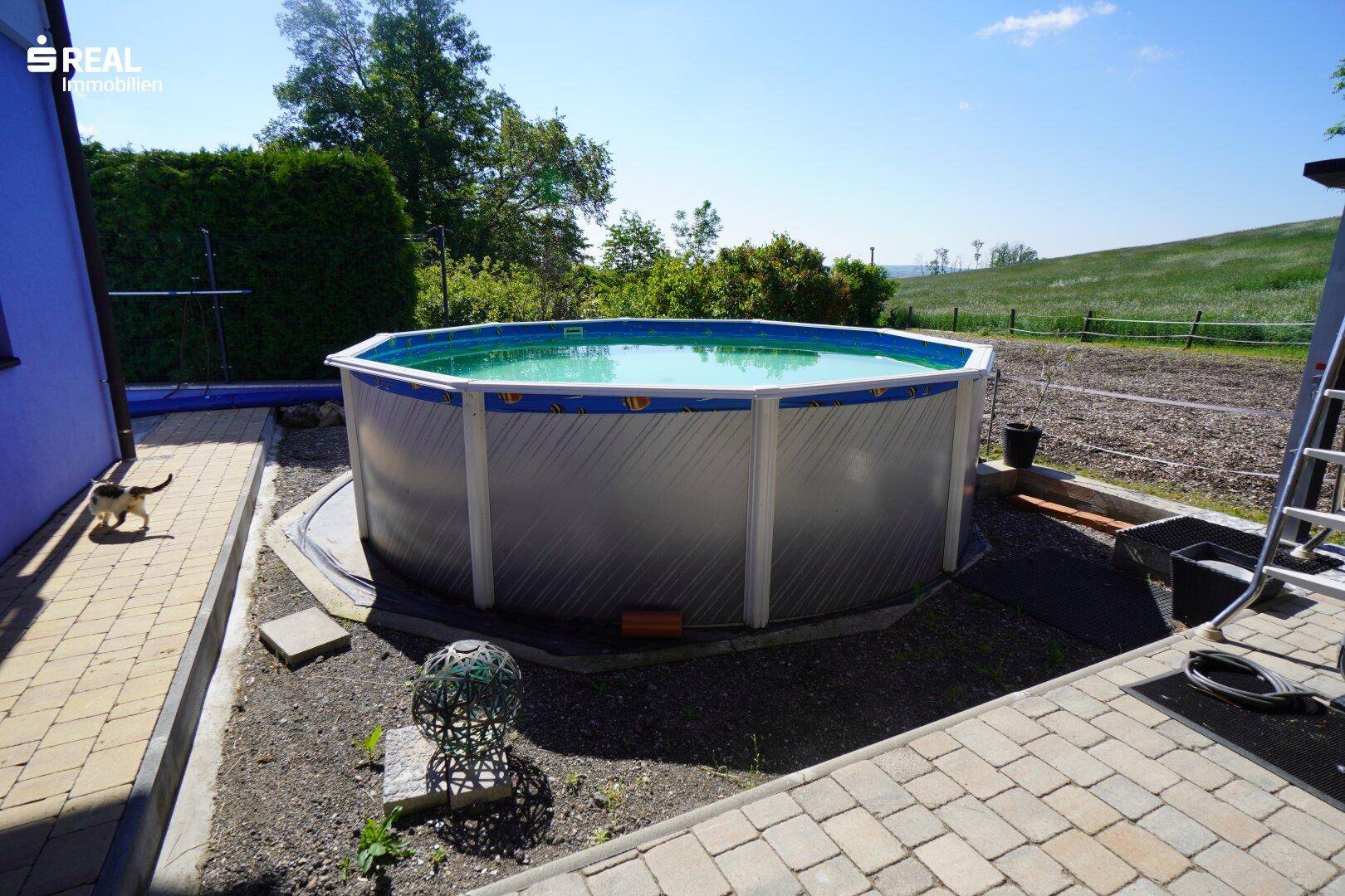 Großer Aufstellpool im Gartenbereich mit Blick auf die umliegende grüne Landschaft.