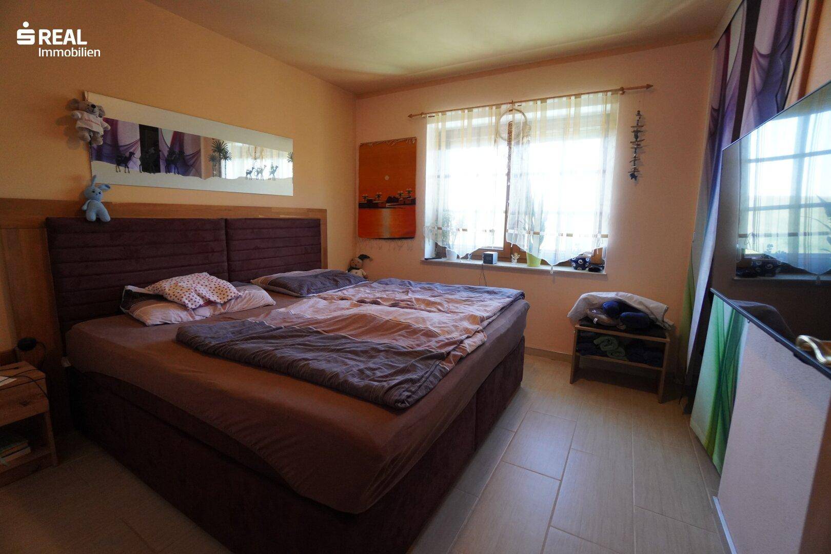 Helles Schlafzimmer mit großem Bett, Fliesenboden und Blick nach draußen.