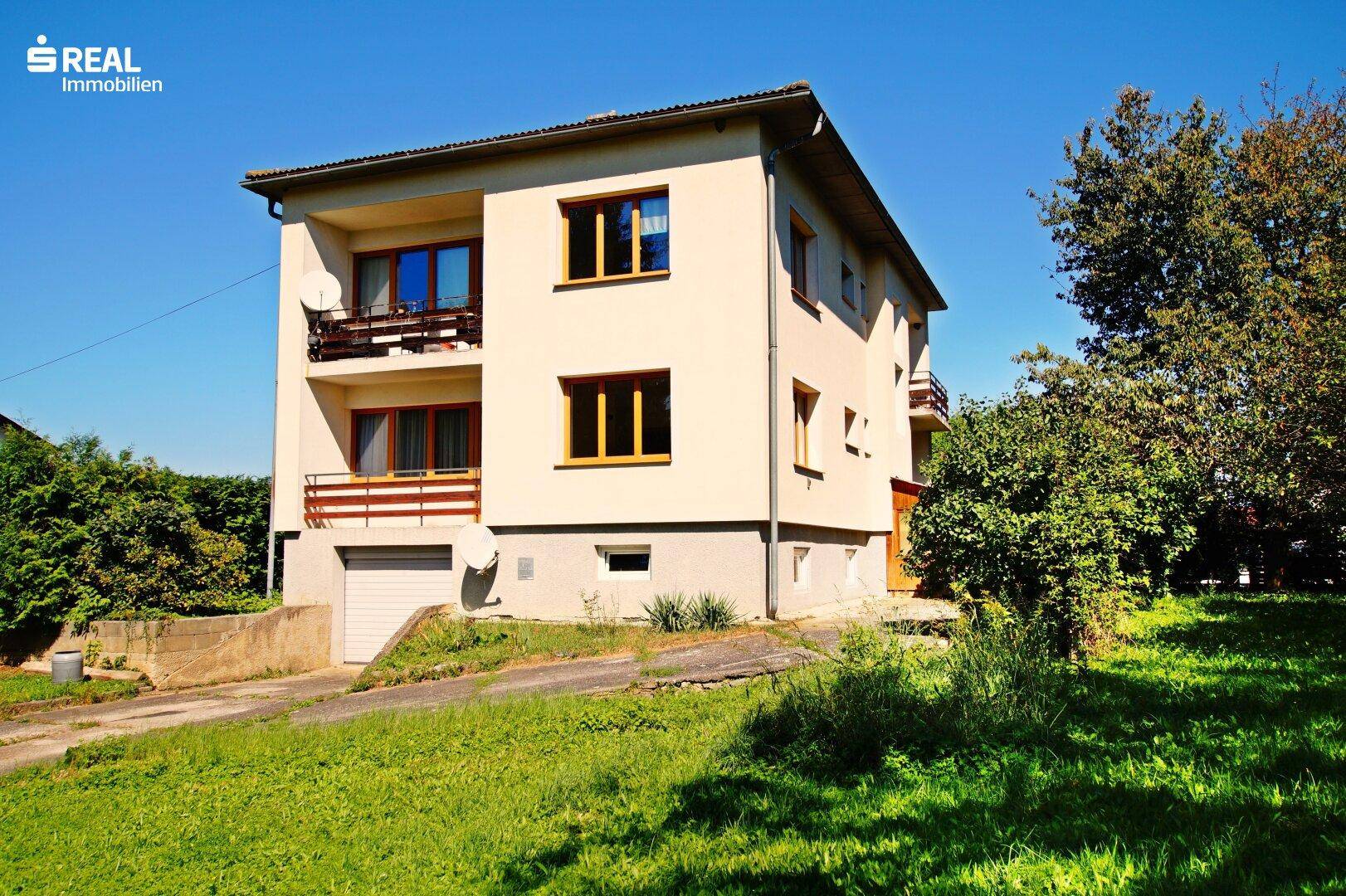 Seitenansicht des Hauses mit Balkonen und der Zufahrt zur Garage, eingebettet in die Natur.