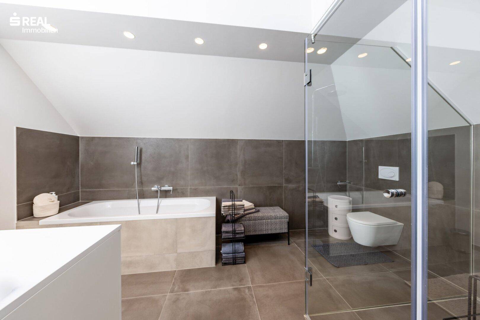 Elegantes Badezimmer mit Badewanne, wandhängendem WC und großformatigen Fliesen.