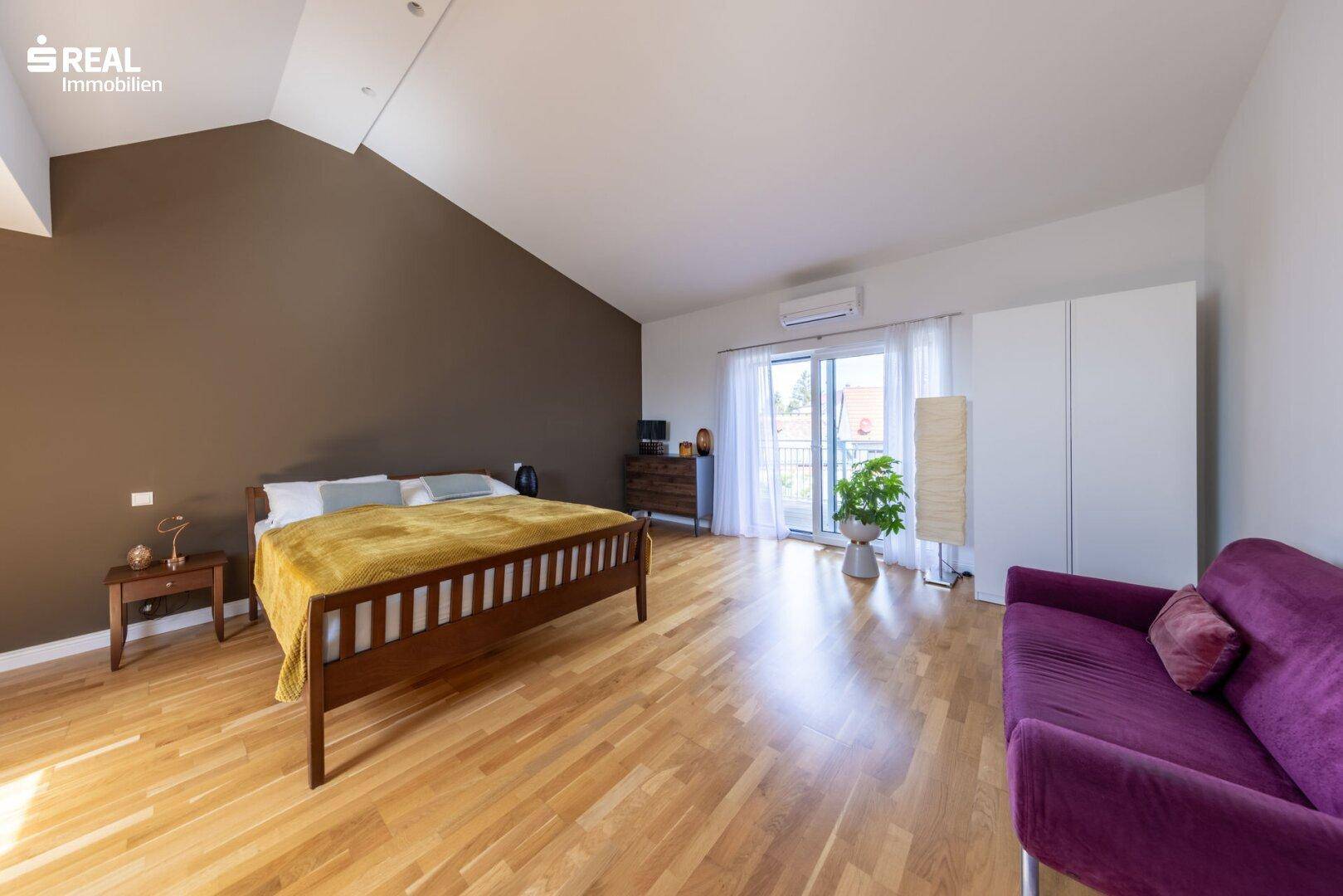 Helles Schlafzimmer mit Holzboden, brauner Akzentwand und Balkonzugang.