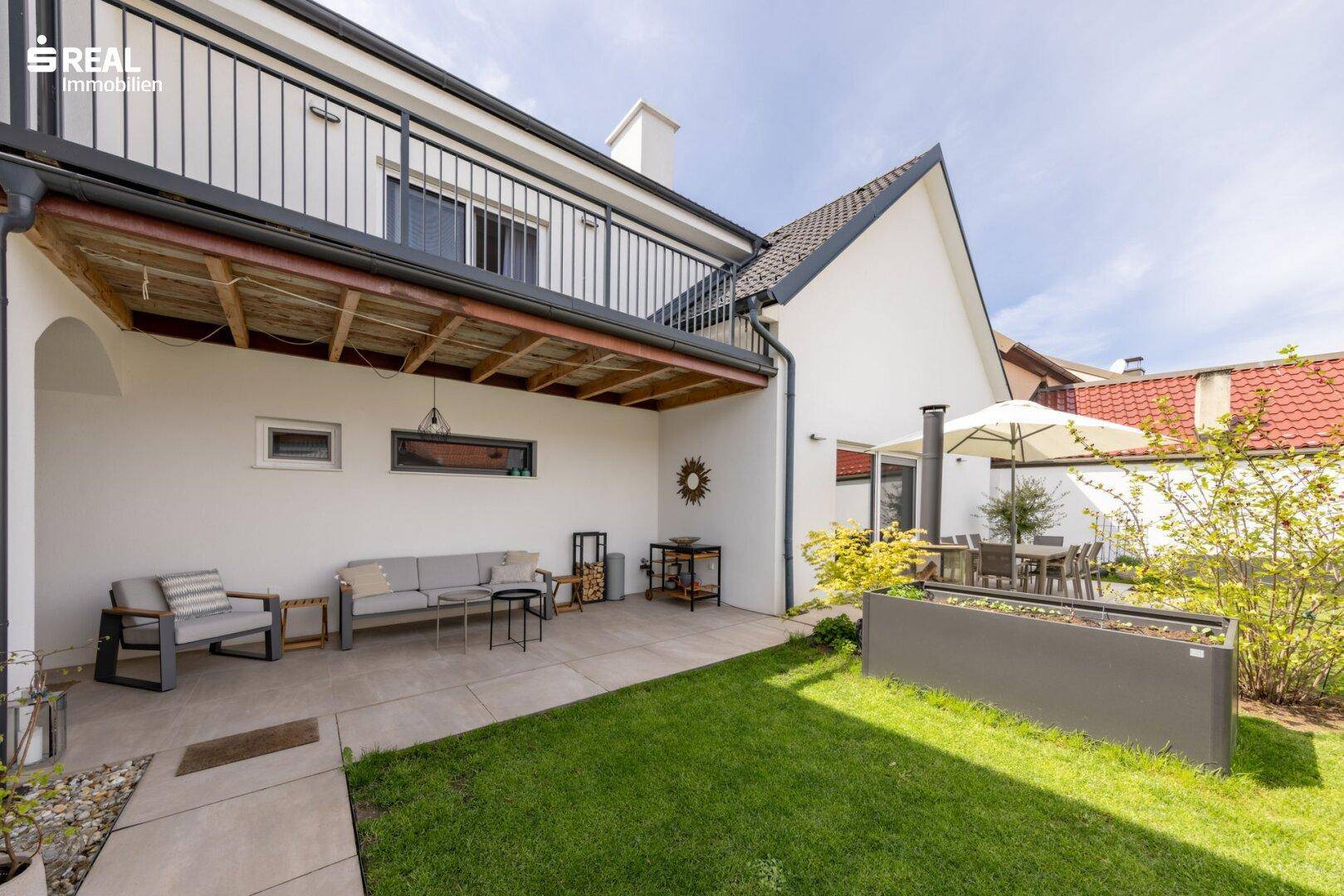 Überdachte Terrasse mit Lounge-Möbeln und angrenzendem Rasenbereich.