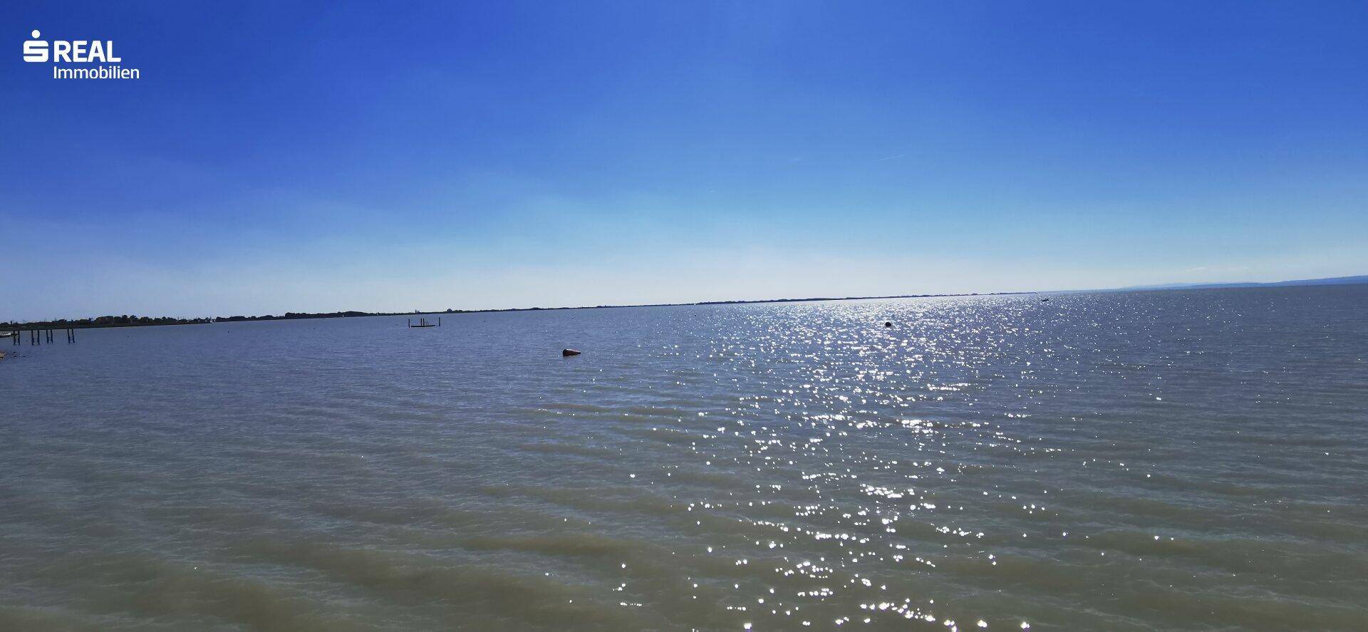 Weitläufiger Blick über eine glitzernde Wasserfläche unter einem strahlend blauen Himmel.