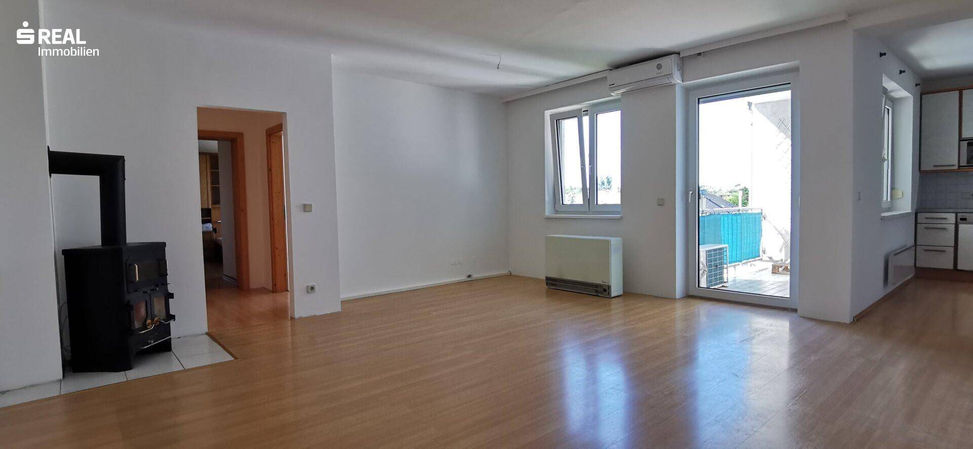 Helles Wohnzimmer mit Holzfußboden, einem Kaminofen und Zugang zu einem Balkon oder einer Terrasse.