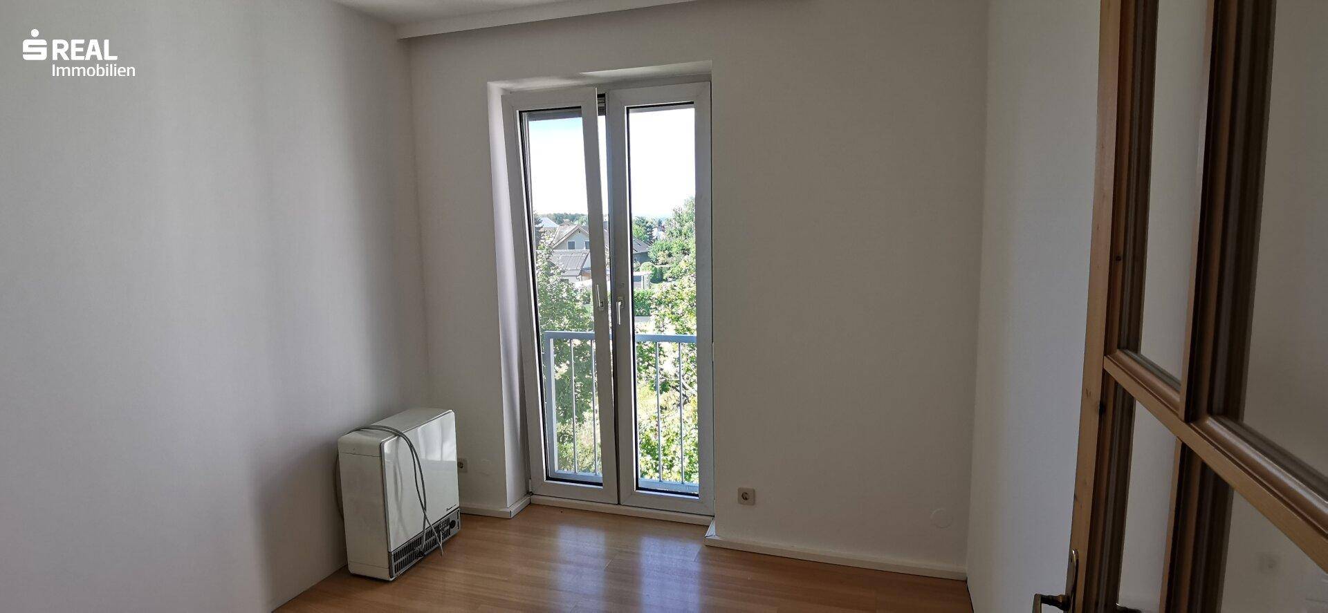 Helles Zimmer mit Holzfußboden und einer großen Fenstertür, die viel Tageslicht hereinlässt.