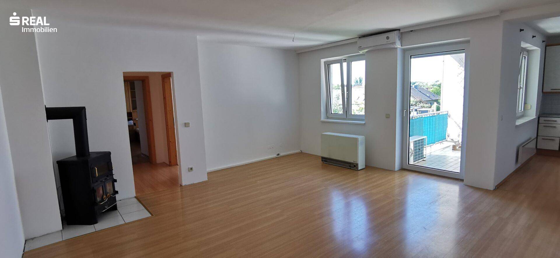 Helles Wohnzimmer mit Holzfußboden, einem Kaminofen und Zugang zu einem Balkon oder einer Terrasse.