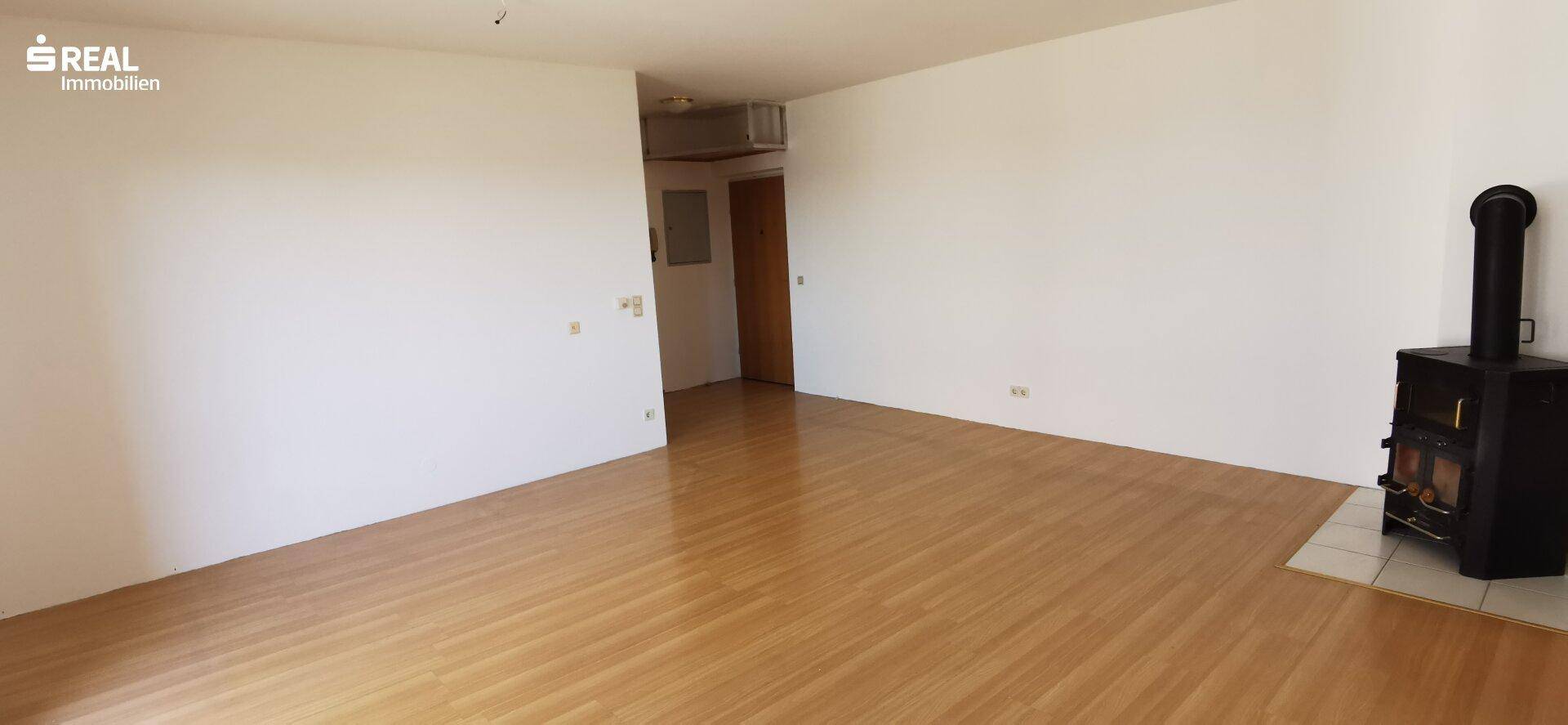 Geräumiges Wohnzimmer mit hellem Holzfußboden und einem gemütlichen Kaminofen als Wärmequelle.