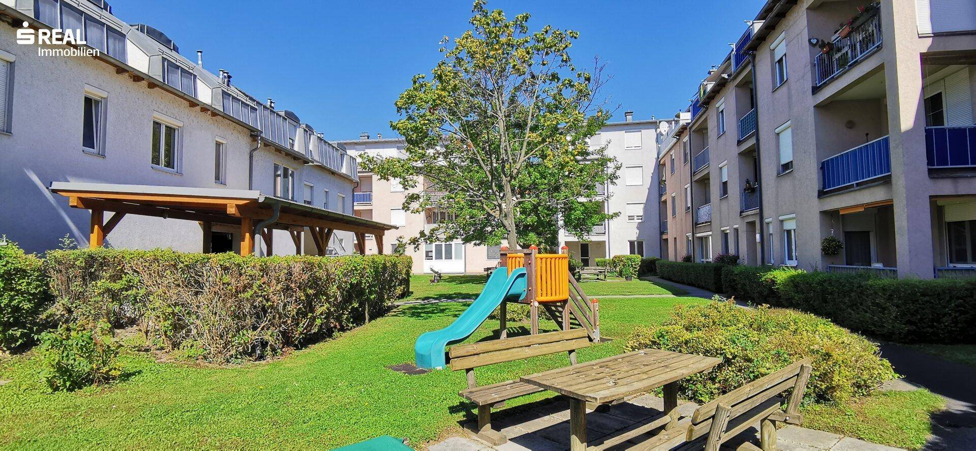 Gepflegter Gemeinschaftsgarten mit Spielplatz, Sitzbänken und viel Grünfläche zwischen den Gebäuden.