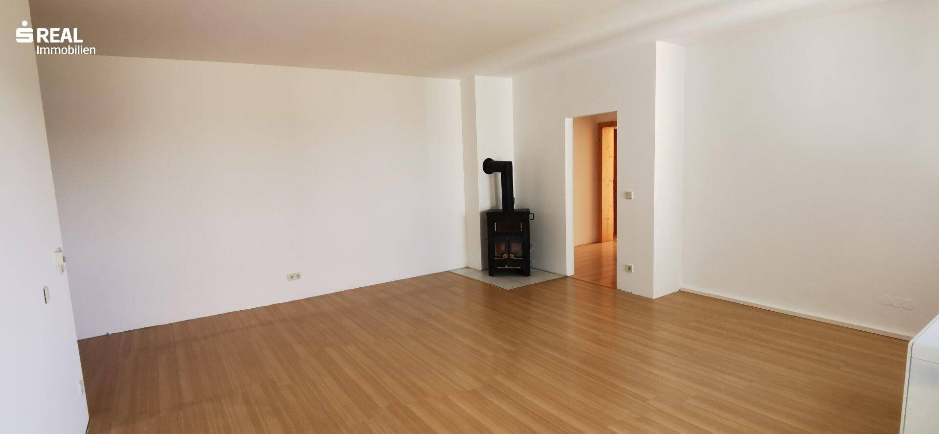 Geräumiges Wohnzimmer mit hellem Holzfußboden und einem gemütlichen Kaminofen als Wärmequelle.