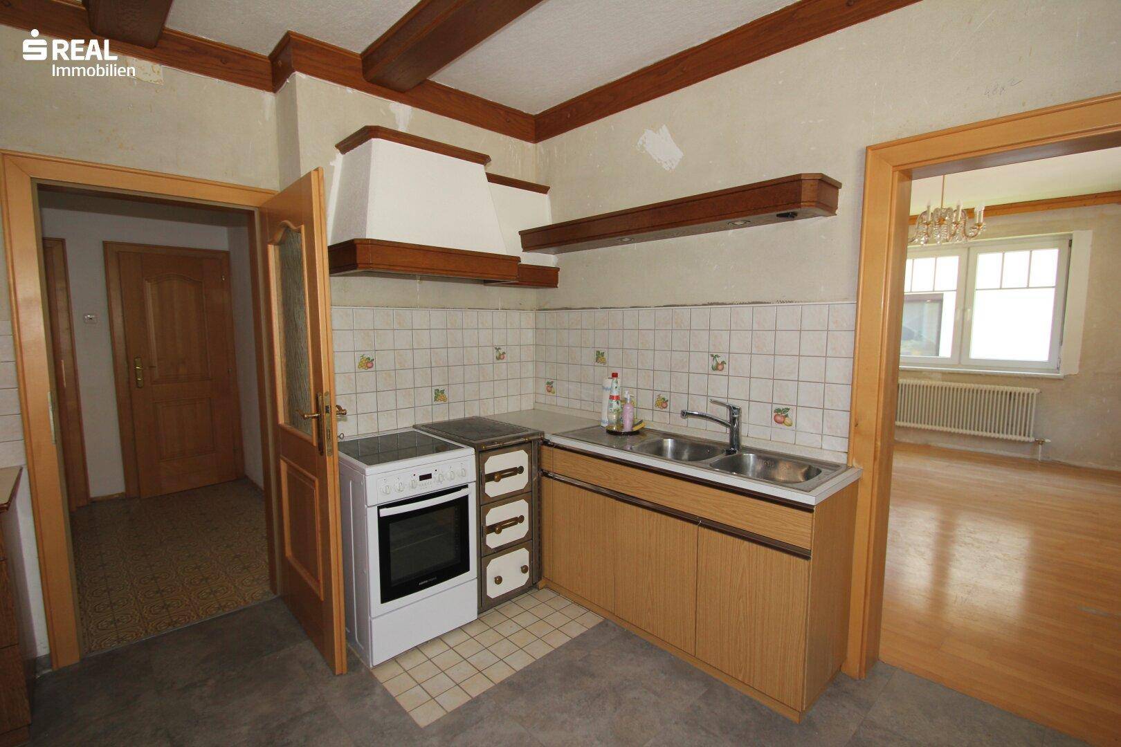 Ältere Küche mit Holzschränken, Fliesenrückwand und sichtbaren Holzbalken an der Decke.