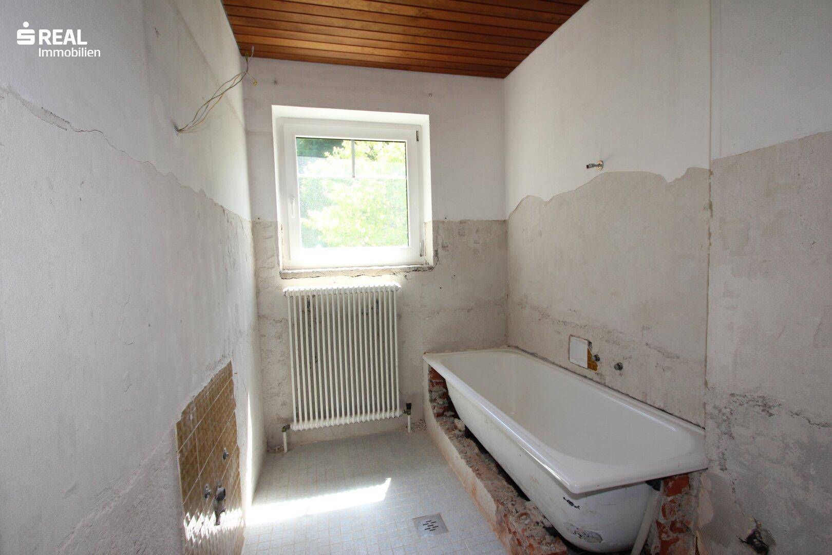 Badezimmer in Renovierung mit Badewanne, Fenster und Holzdecke, noch unfertig.