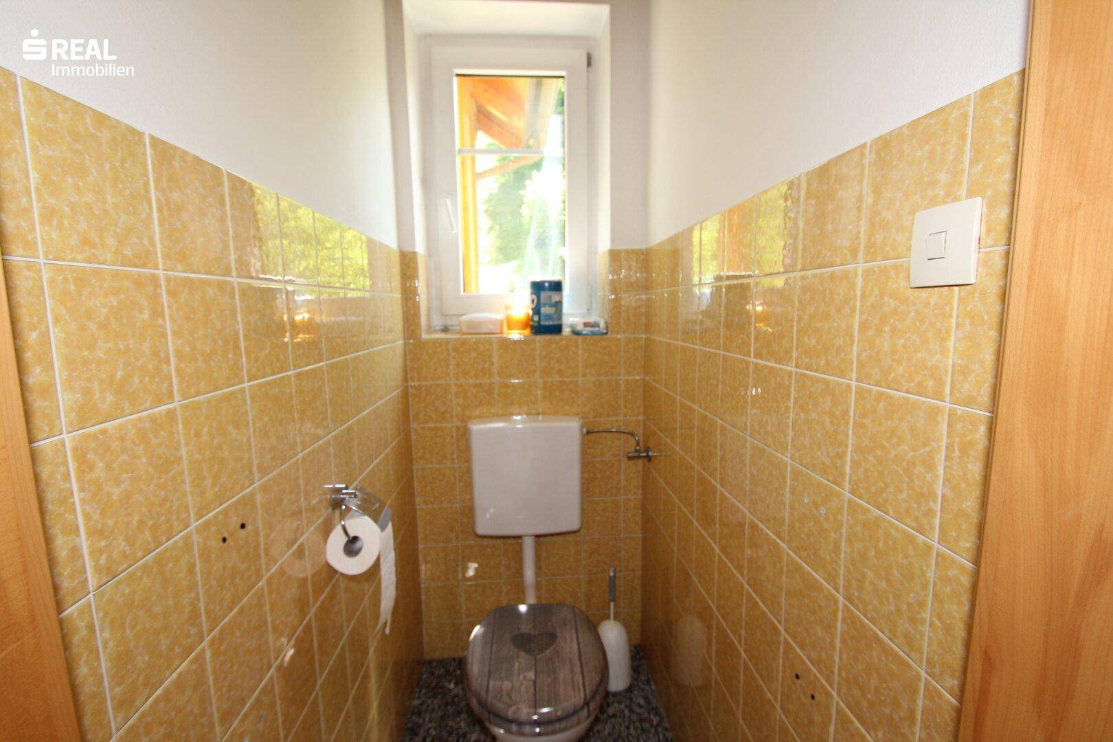 Separate Toilette mit gelben Fliesen, Fenster und einfacher Ausstattung, funktional.