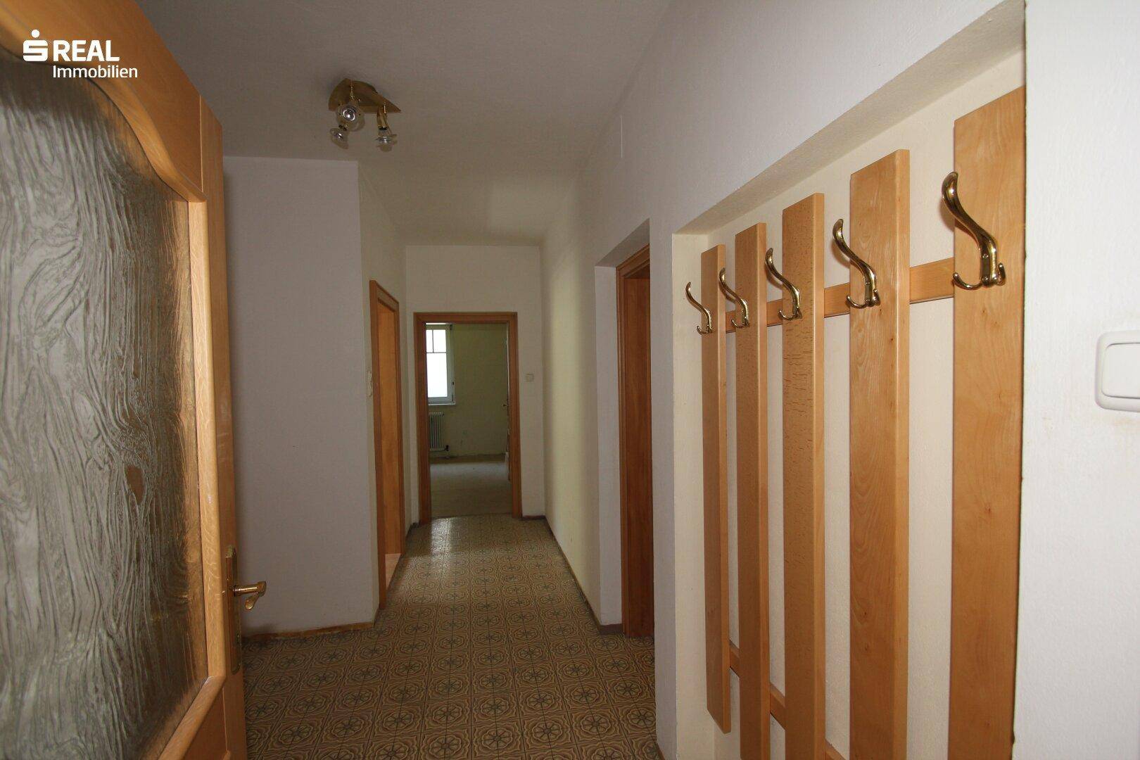 Flur mit gemustertem Boden, Holztüren und Garderobe, verbindet verschiedene Räume.