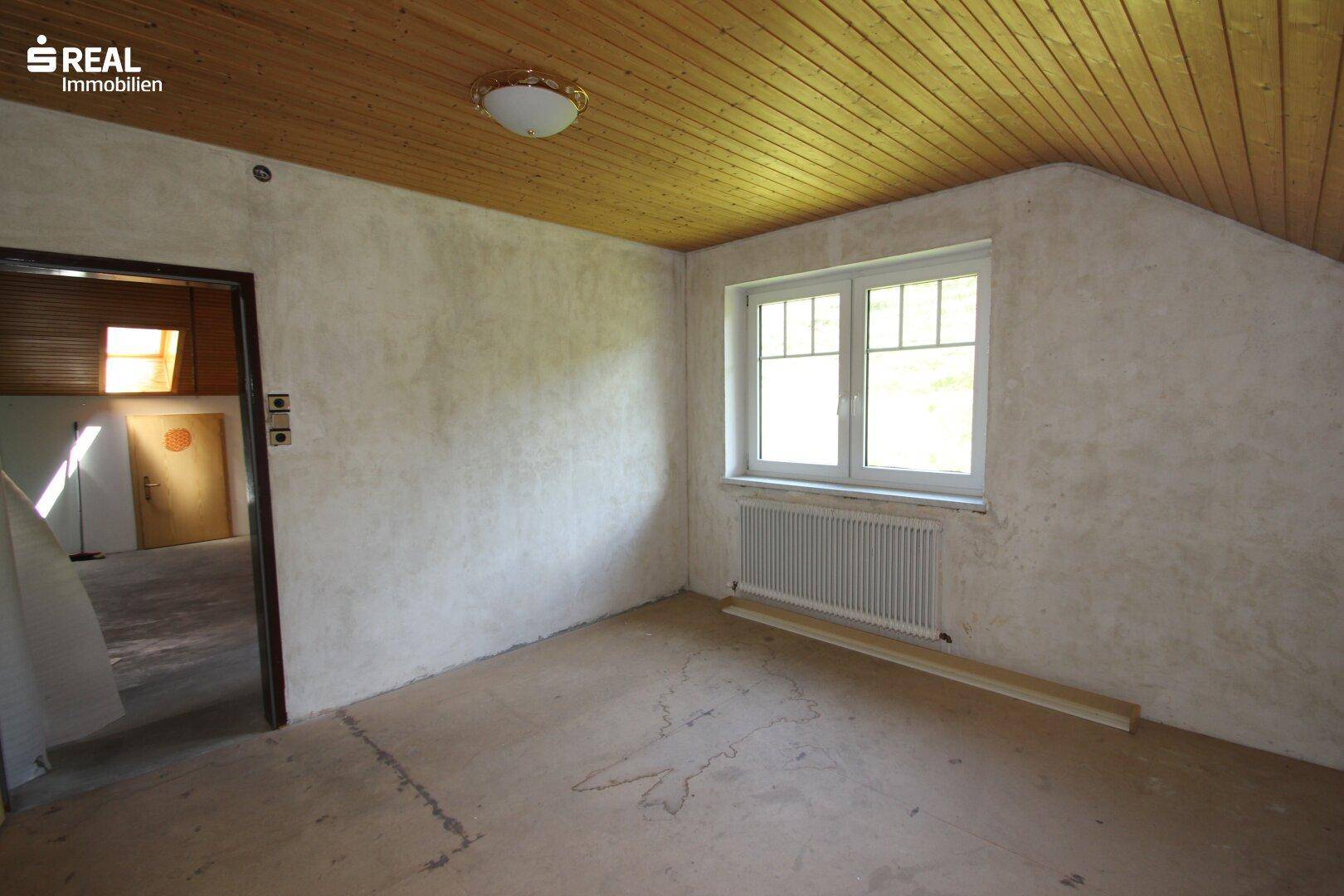 Dachzimmer mit Holzdecke, Fenster und Heizkörper, bereit für die individuelle Gestaltung.