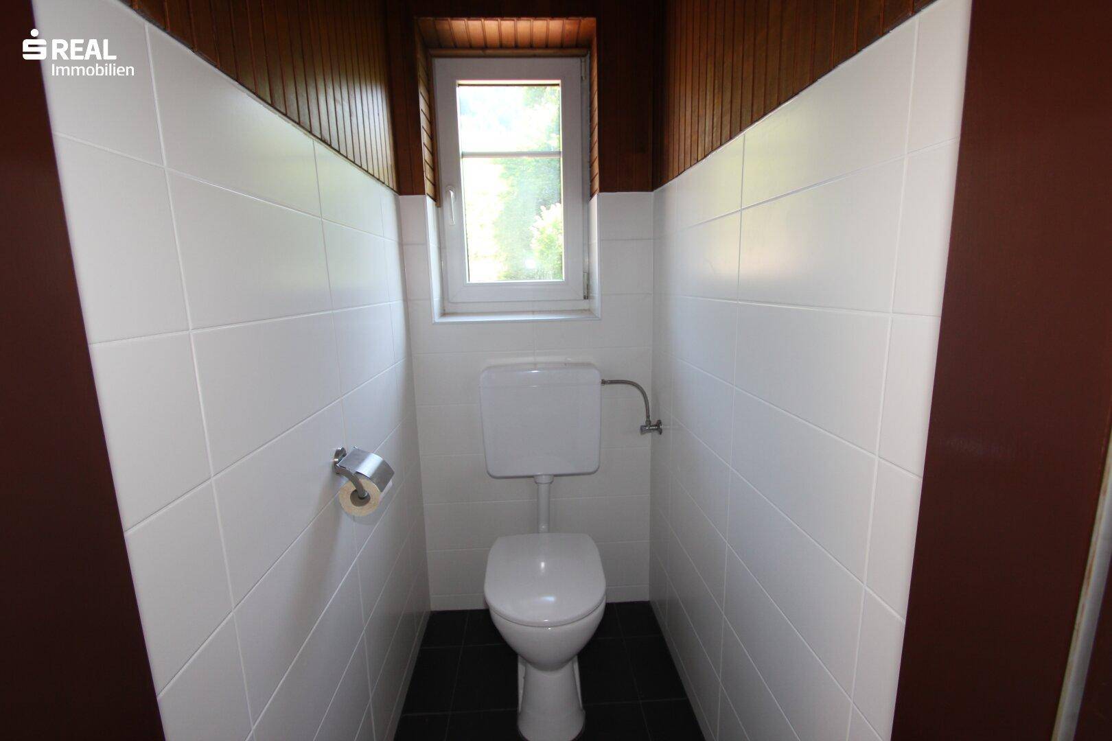 Separate Toilette mit weißen Fliesen und Holzverkleidung, funktional und sauber.