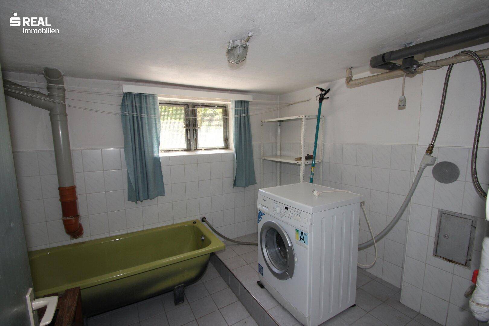 Waschküche im Keller mit Waschmaschine, Wanne und Fenster, praktisch eingerichtet.