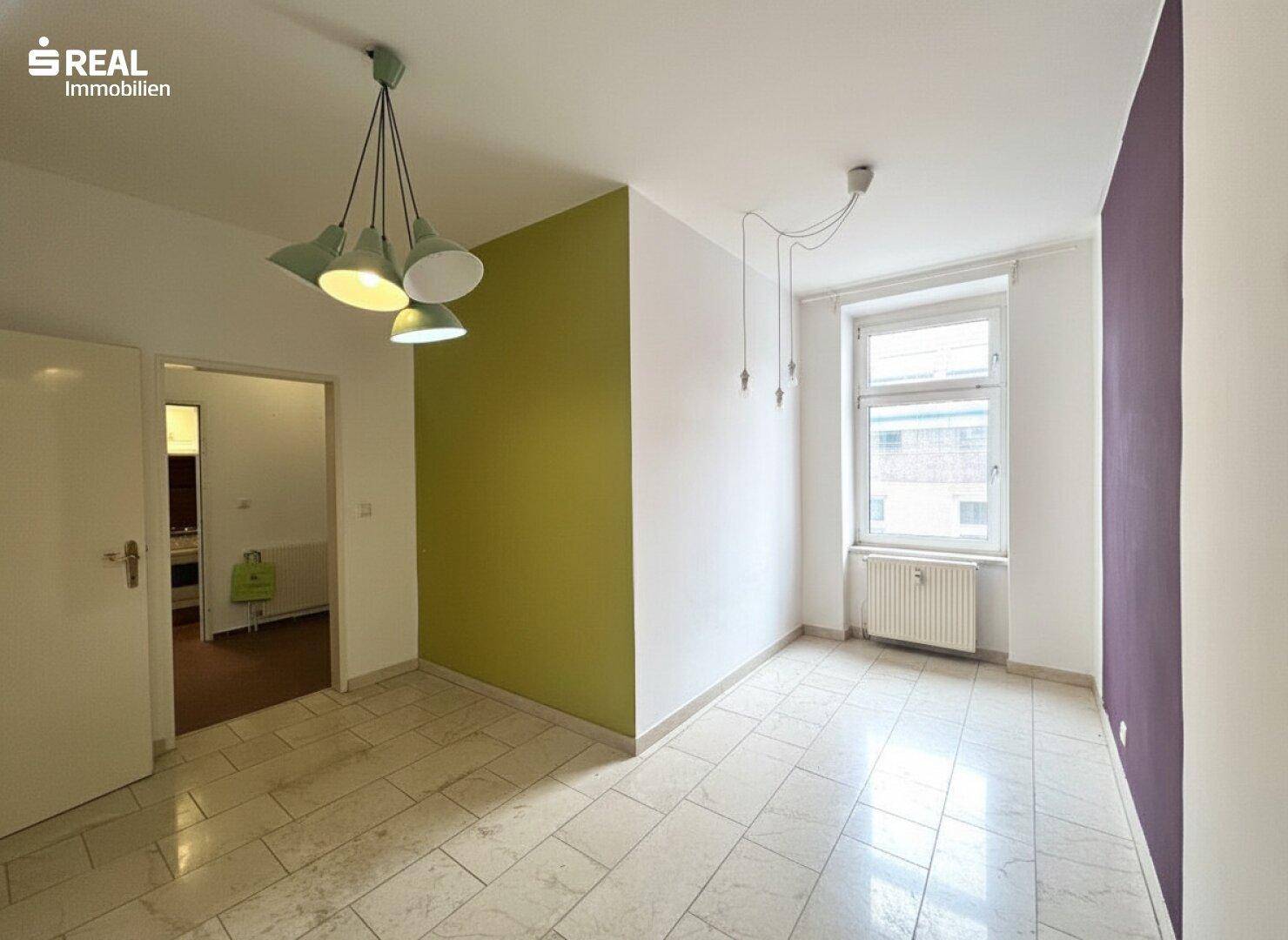 Leerer Raum mit Fliesenboden, Akzentwänden in Grün und Violett sowie moderner Deckenbeleuchtung.