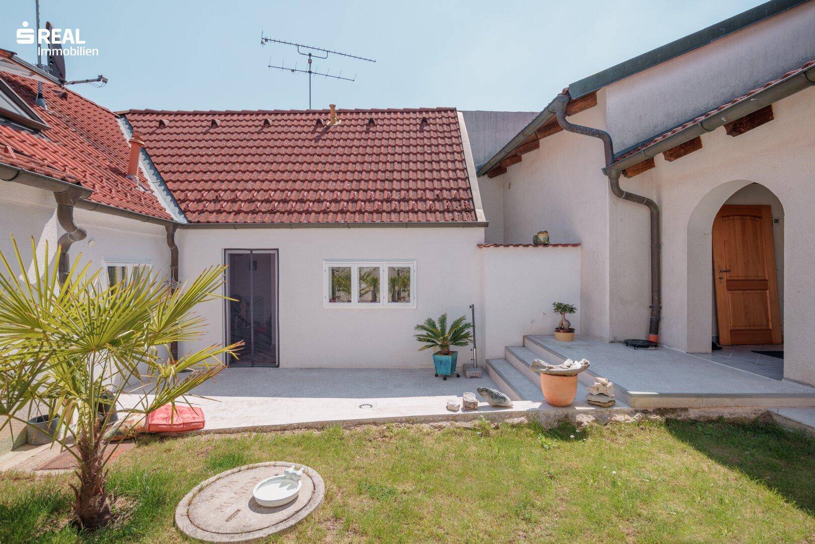 Innenhof mit Rasenfläche, gepflastertem Bereich und Zugang zu verschiedenen Gebäudeteilen des Hauses.