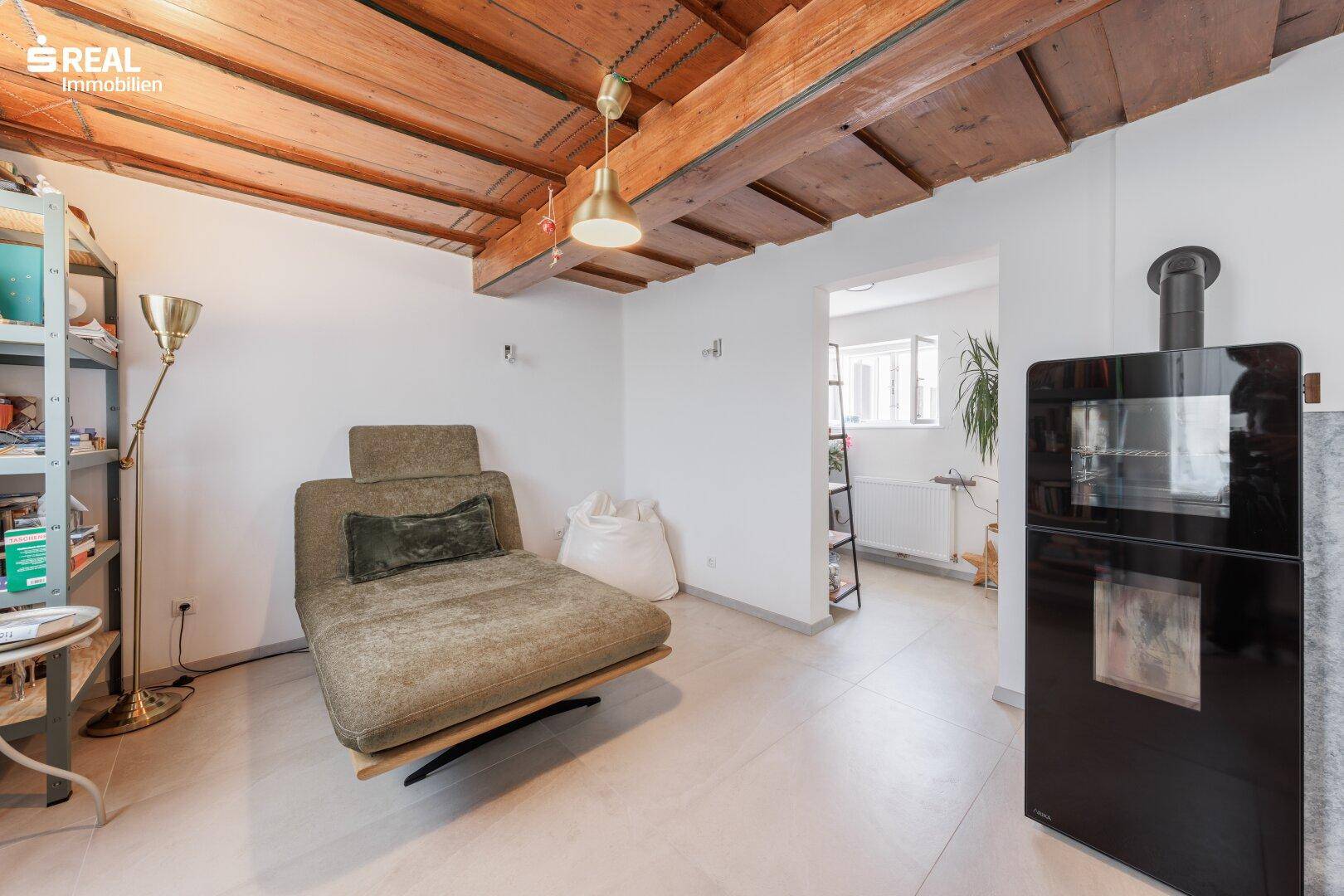 Wohnzimmer mit Holzbalkendecke, hellem Boden und modernem Kaminofen für gemütliche Abende.