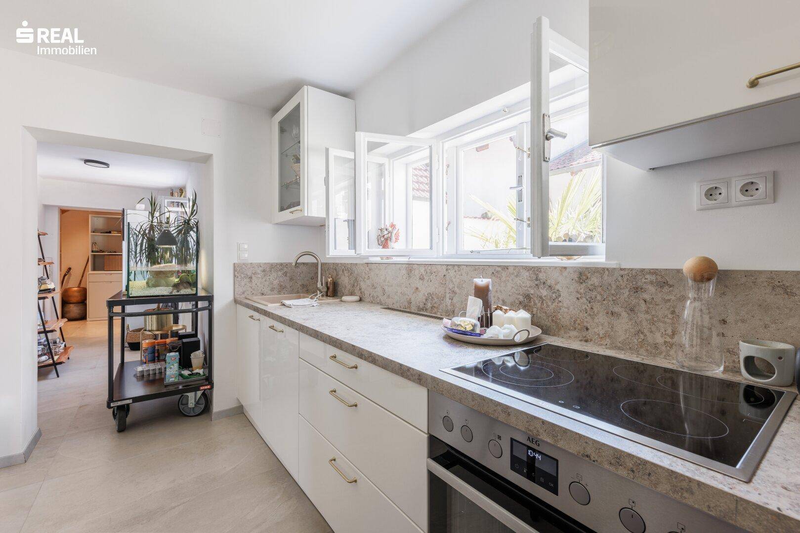 Moderne Küche mit weißen Schränken, Stein-Arbeitsplatte und Fensterblick, ideal zum Kochen.