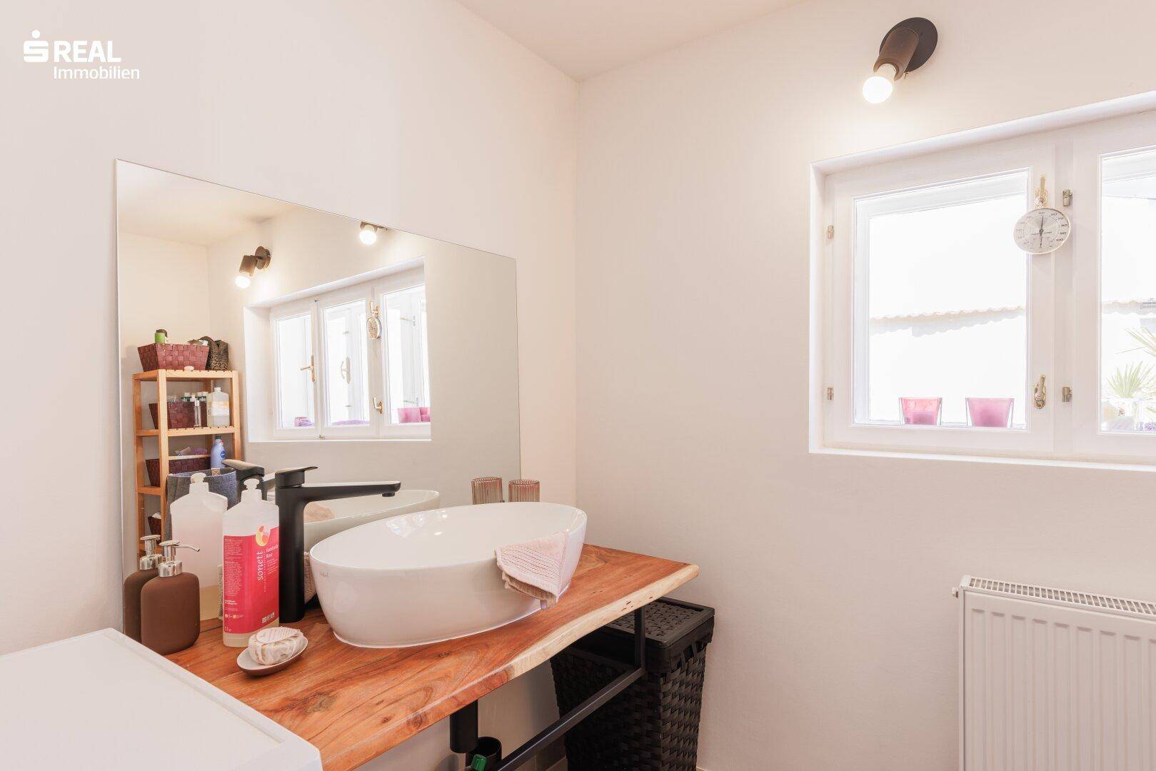 Badezimmer mit modernem Aufsatzwaschbecken, Holzplatte und Fenster, hell und funktional gestaltet.