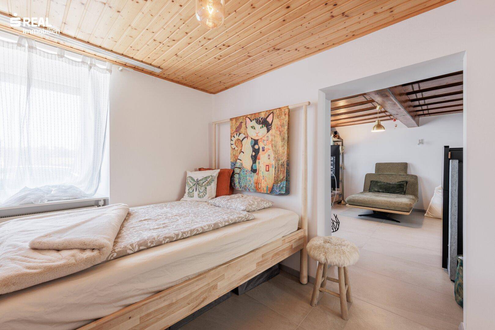 Schlafzimmer mit Holzbett, Holzdecke und Blick in den angrenzenden Wohnbereich, hell und einladend.