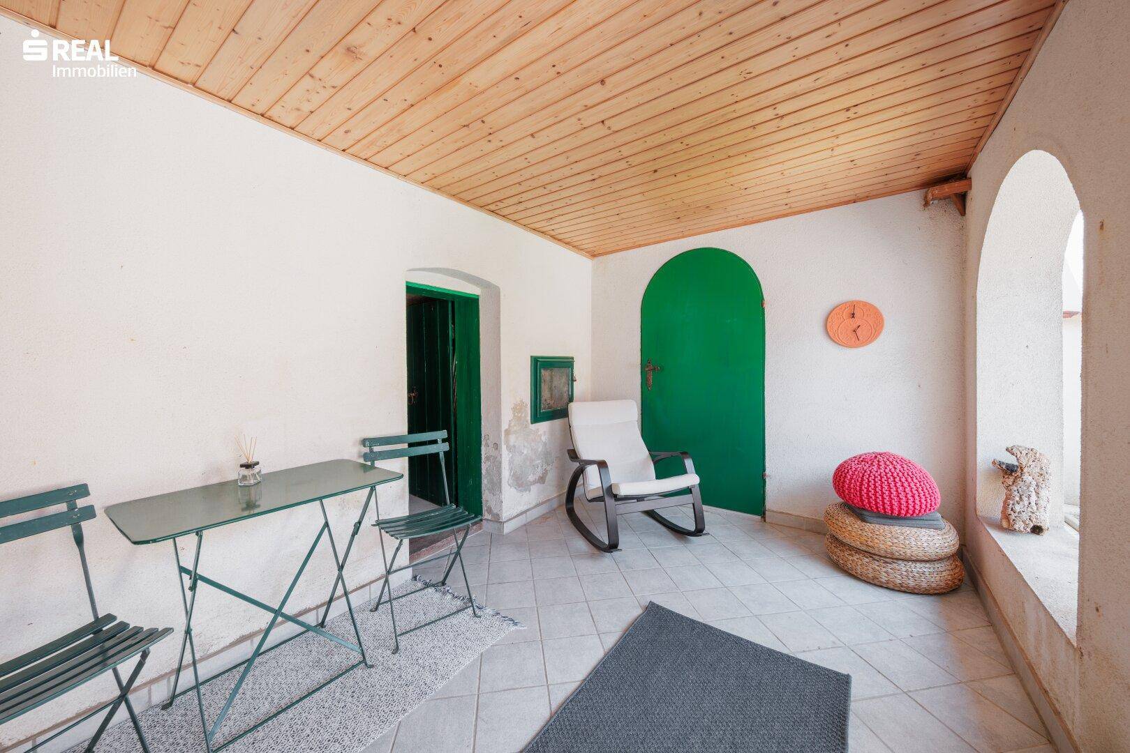 Gemütliche Loggia mit Fliesenboden, Holzdecke und grünen Akzenten für entspannte Stunden im Freien.