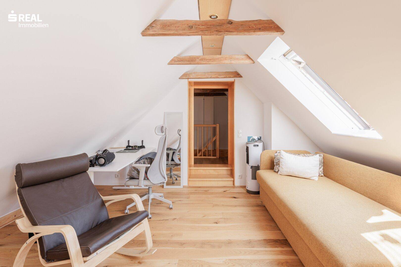 Helles Dachzimmer mit Holzboden, Dachfenstern und sichtbaren Holzbalken, ideal als Büro oder Wohnraum.