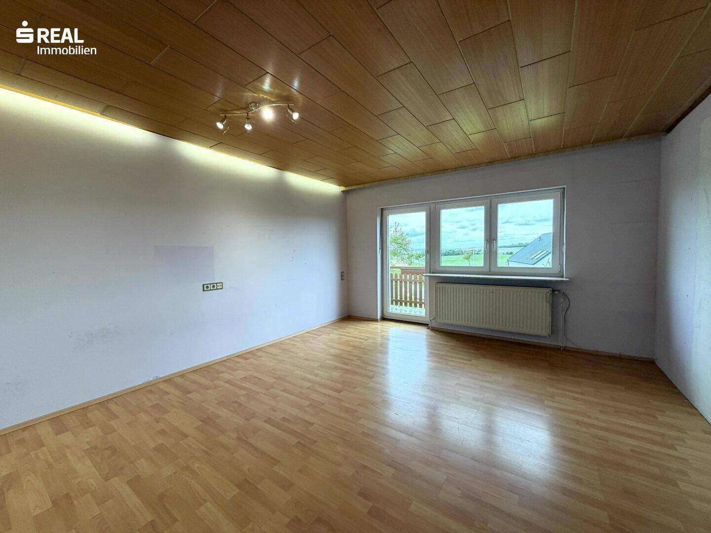 Geräumiges Zimmer mit Laminatboden, Holzdecke und Zugang zu einem kleinen Balkon.