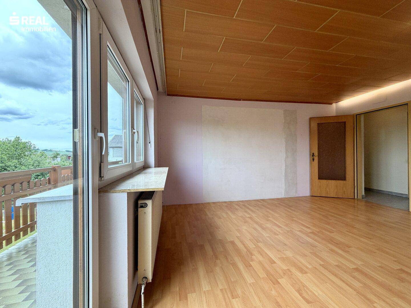 Helles Zimmer mit Balkonzugang, Laminatboden und Blick auf die umliegende Landschaft.