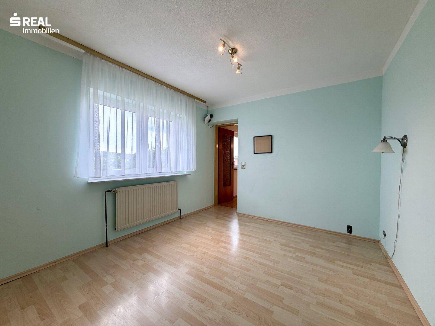 Gemütliches Schlafzimmer mit Laminatboden, hellblauen Wänden und großem Fenster.
