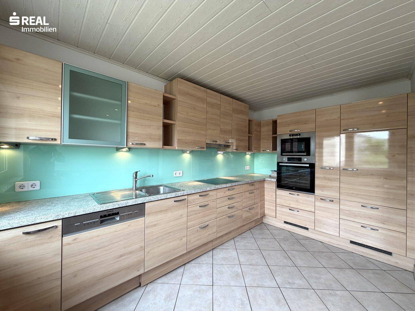 Moderne Einbauküche mit hellen Holzfronten, Granitarbeitsplatte und integrierten Geräten.