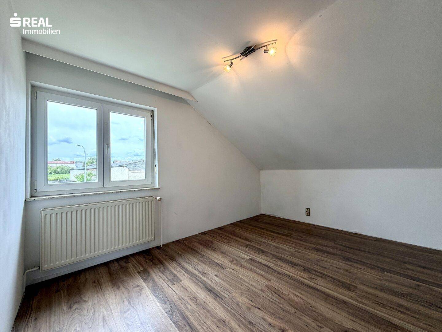 Dachgeschosszimmer mit Laminatboden, schrägen Wänden und Fenster mit Ausblick.