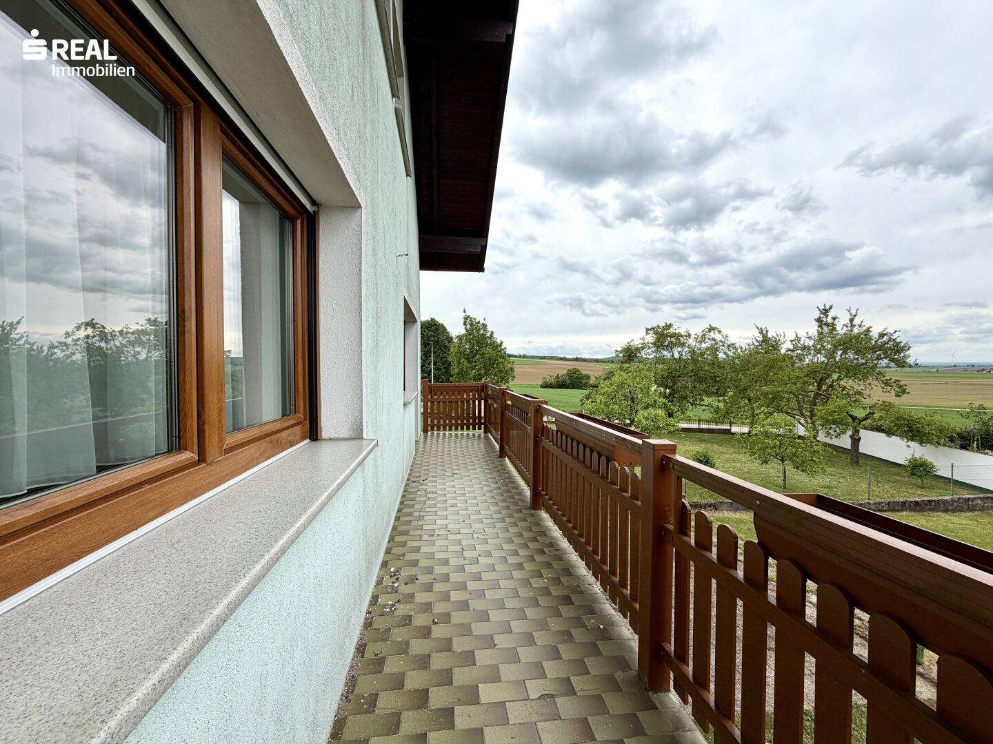 Langer Balkon mit Fliesenboden und Holzgeländer, bietet weite Aussicht auf die Landschaft.